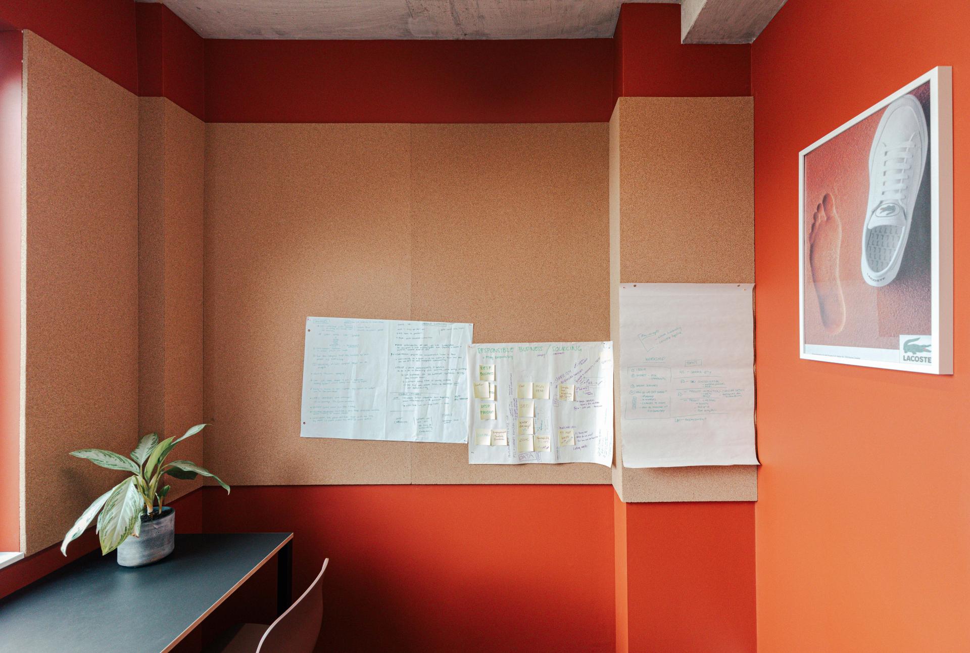 Modern workspace showcasing a cork wall, desk, plant, and Lacoste sneaker poster, reflecting New York warehouse design aesthetics.