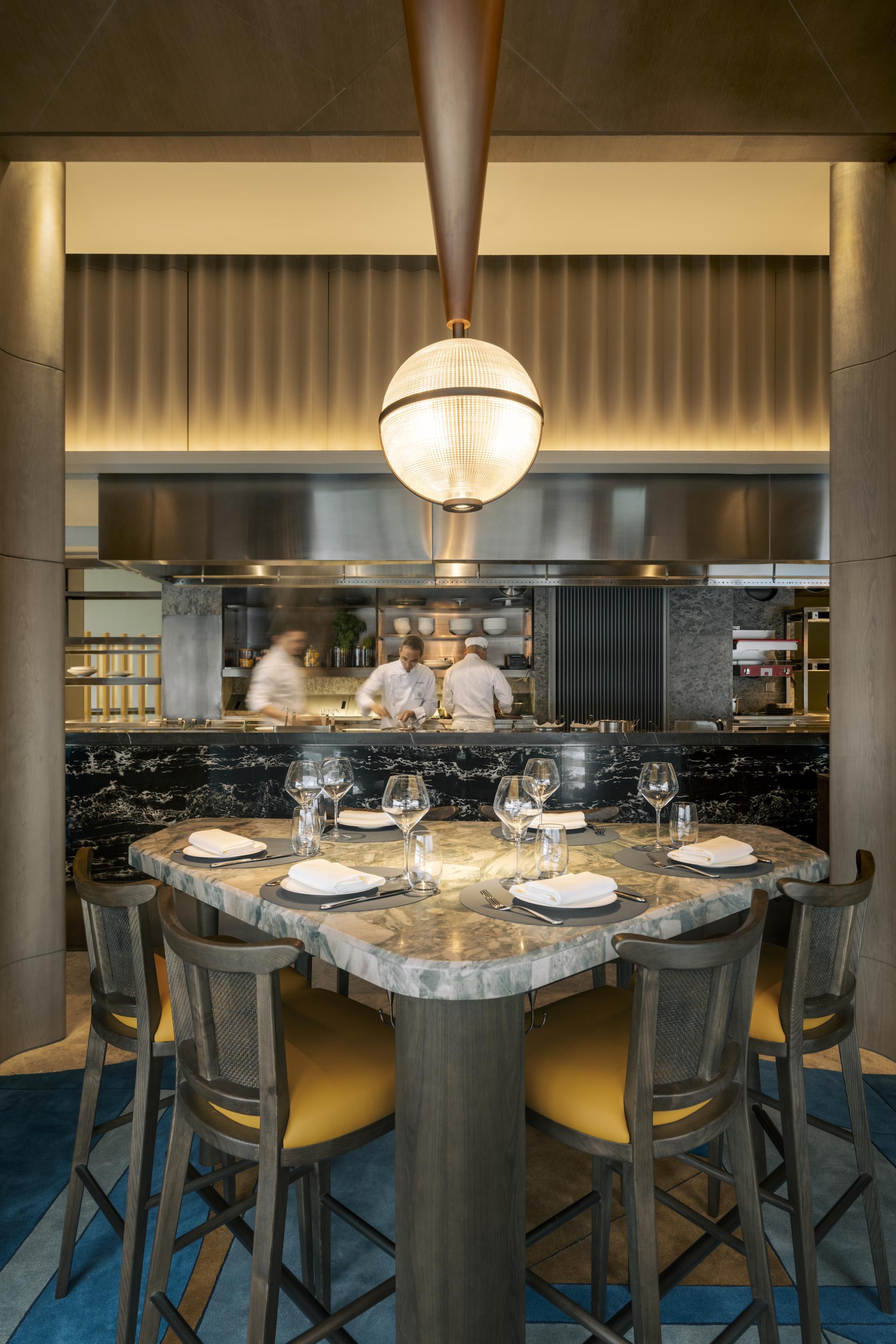 Elegant dining area with Art Deco design, featuring a marble table, stylish chairs, and an open kitchen backdrop.