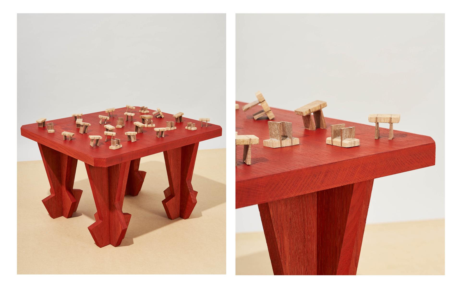 Bold red table features intricate woodwork and small wooden models, exemplifying Dharma Taylor's collaboration with Paul Smith.