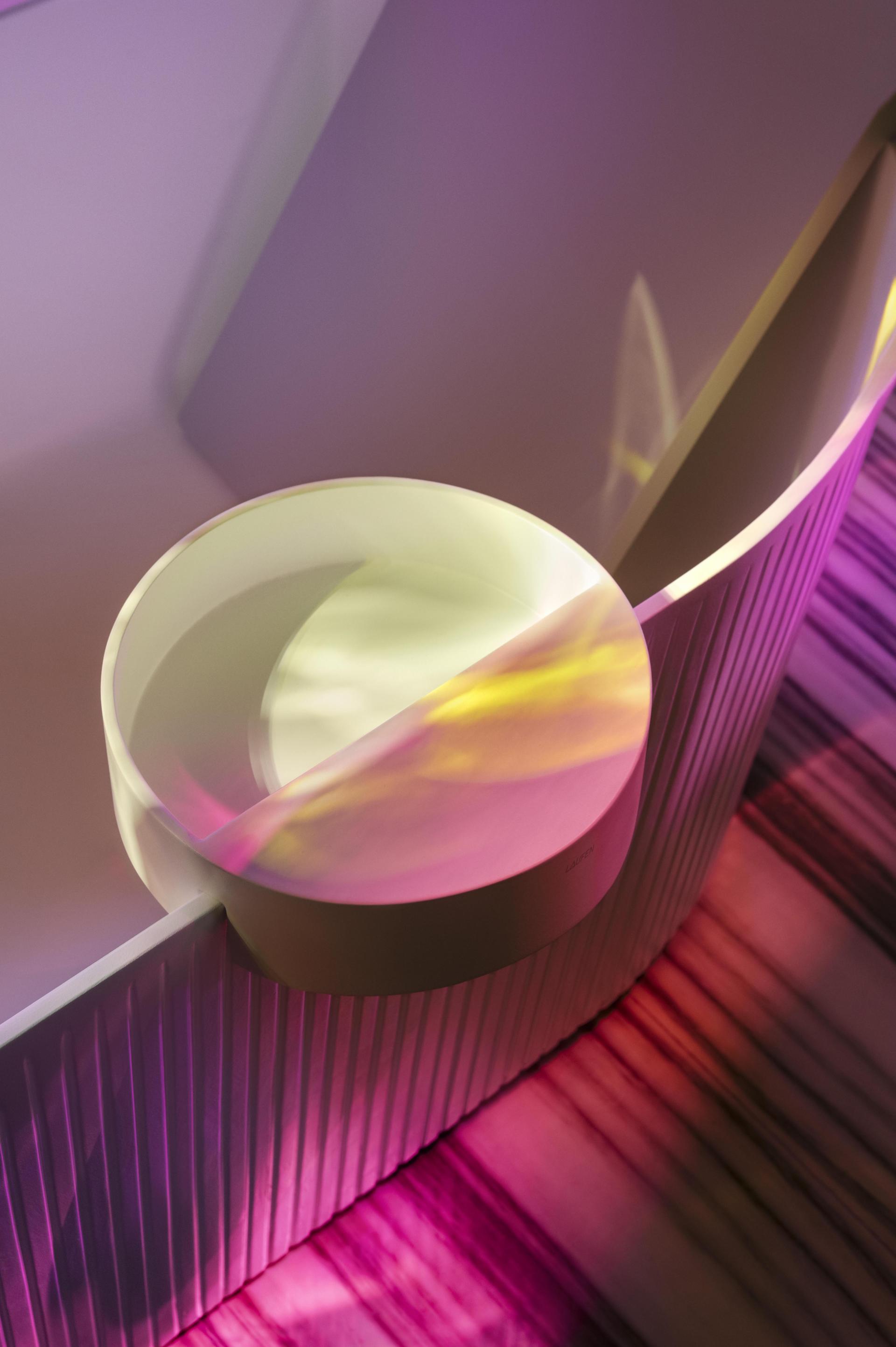 Modern LAUFEN bathtub with sleek design featuring soft curves and vibrant lighting reflections on textured surface.