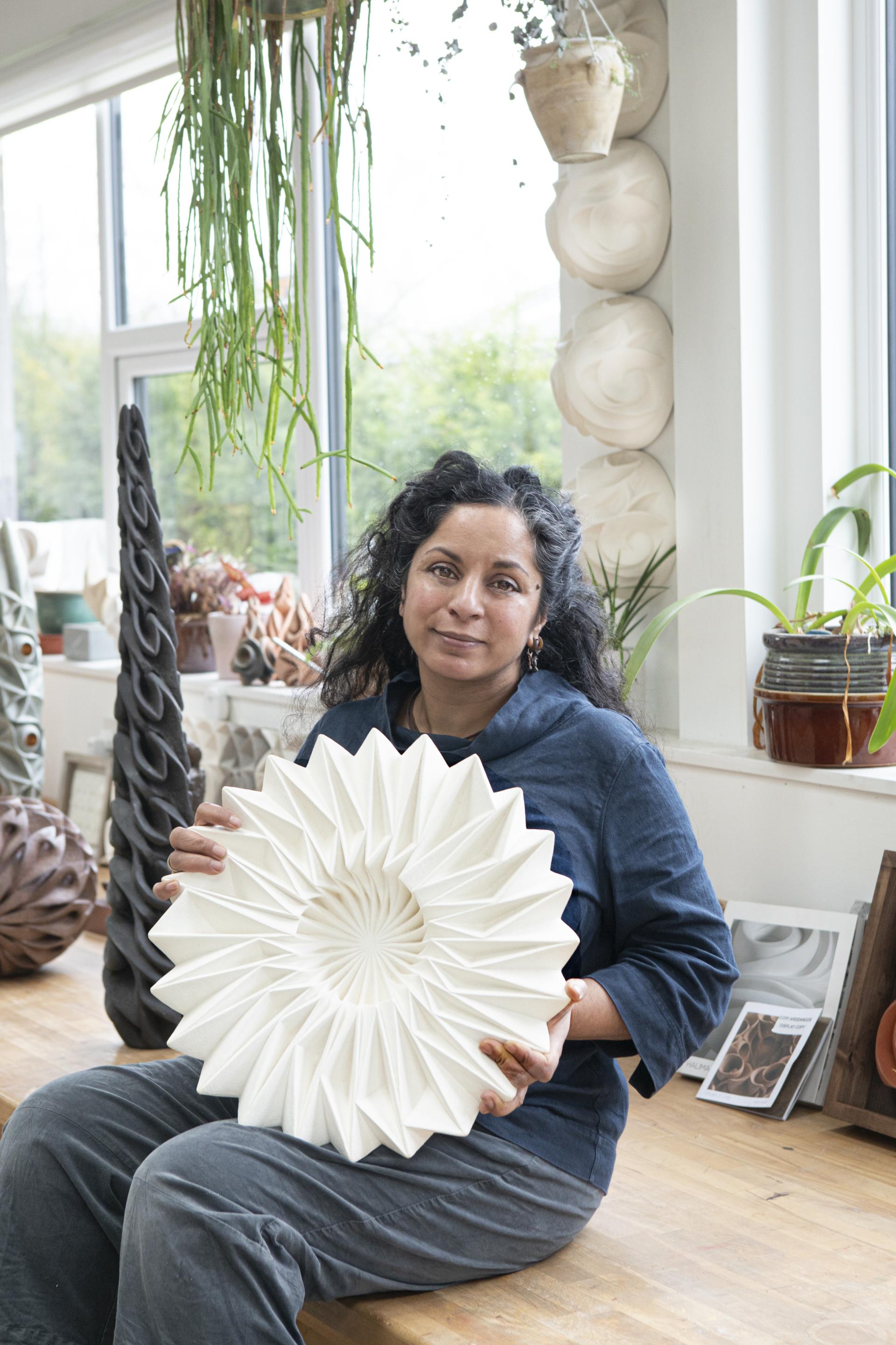 Halima Cassell poses with a sculptural, intricately carved ceramic piece in her artistic studio.