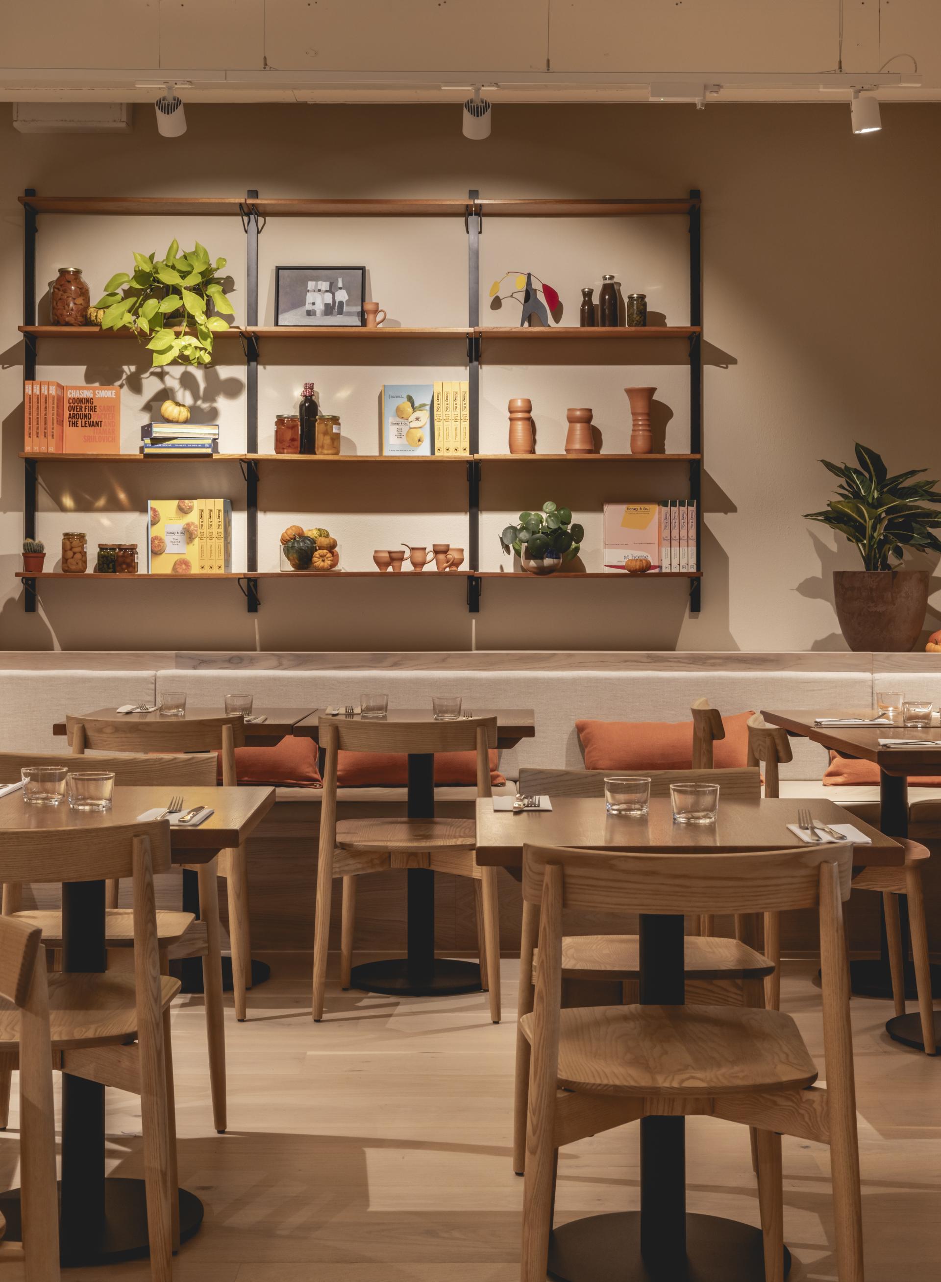 Warm-toned dining area featuring wooden tables and shelves adorned with terracotta decor, books, and plants.