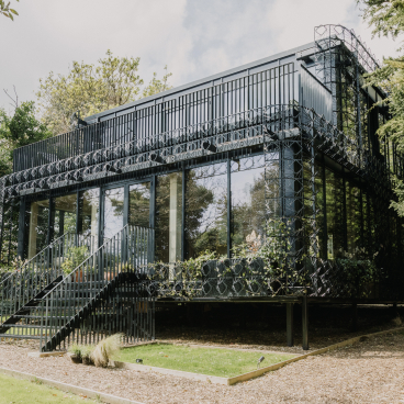 Modern residential architecture featuring handcrafted sculptural surfaces, surrounded by lush greenery in a natural setting.