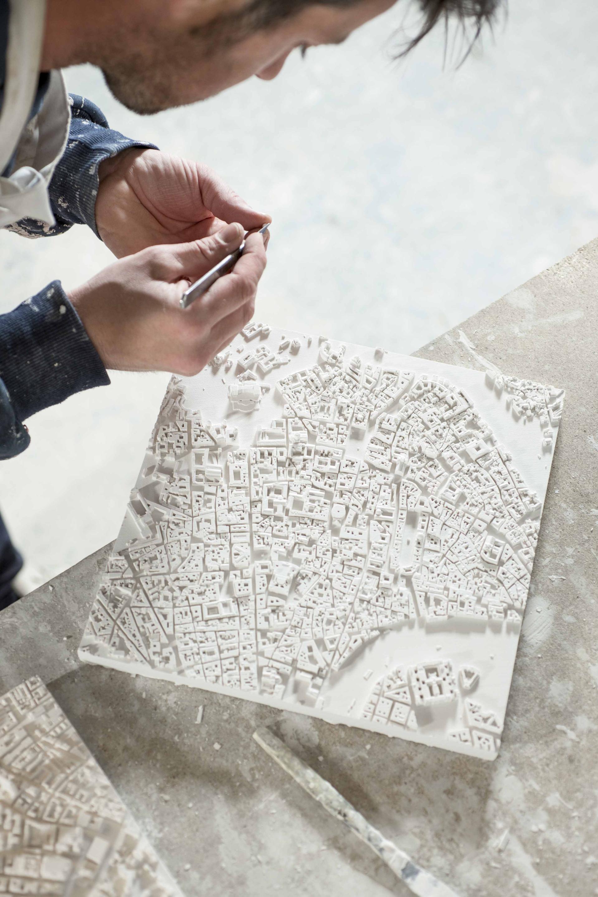 Artist meticulously sculpting a detailed three-dimensional city model, showcasing urban landscape features with precision.