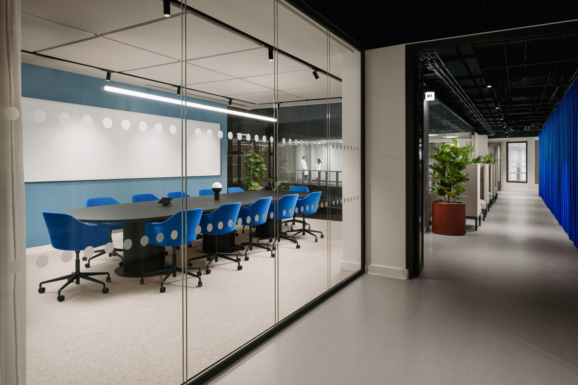 Modern office interior featuring a glass-walled meeting room with blue chairs, designed for collaboration and creativity.