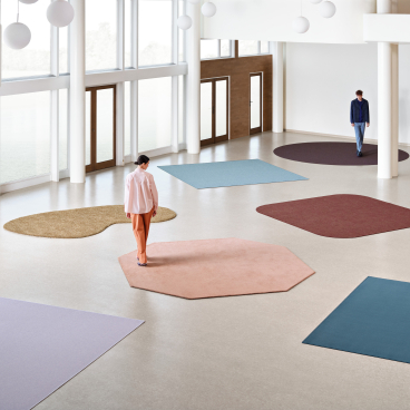 Modern workspace with unique rugs in various shapes, showcasing sustainable design concepts at Orgatec 2024.