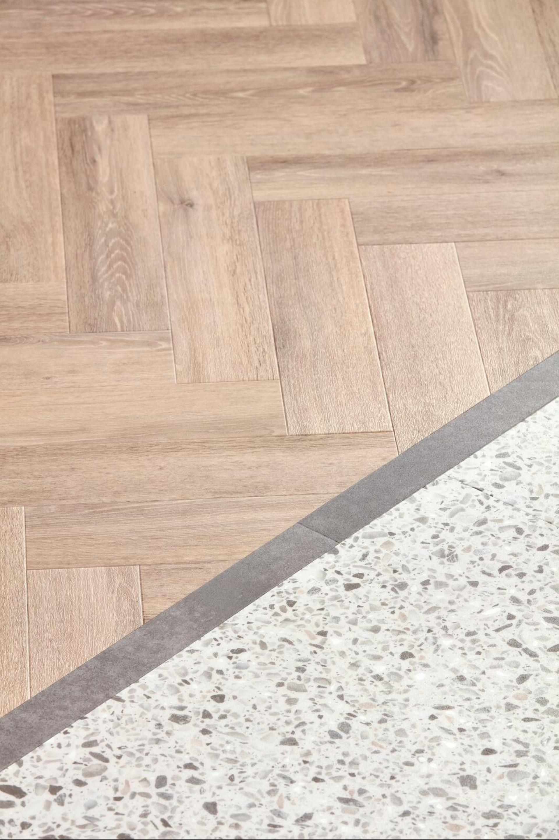 Two flooring materials, one resembling light wood in a herringbone pattern and the other features a speckled, concrete-like surface.