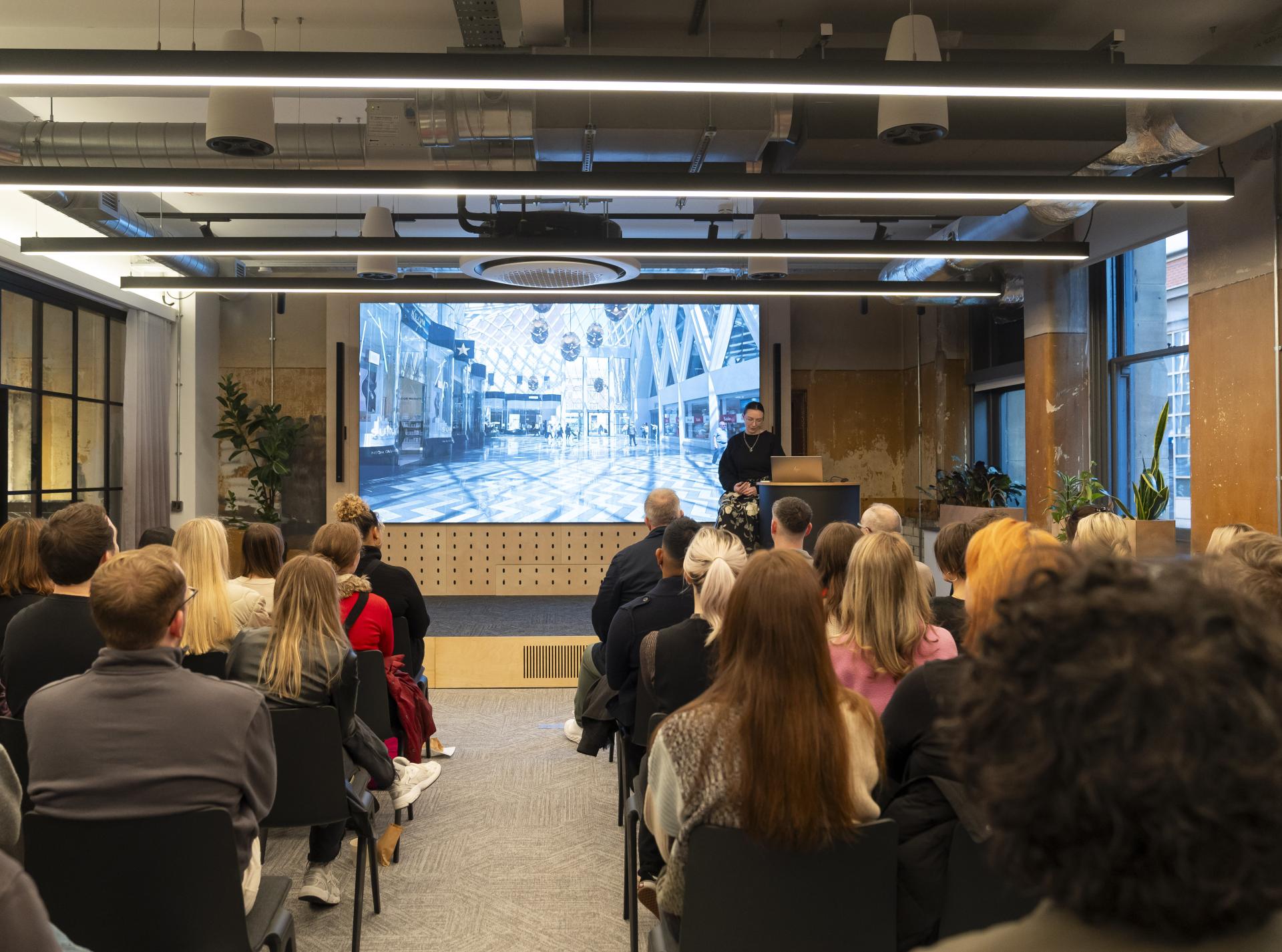 Audience at a presentation on inclusive design, featuring a speaker discussing neurodiversity and accessibility in architecture.