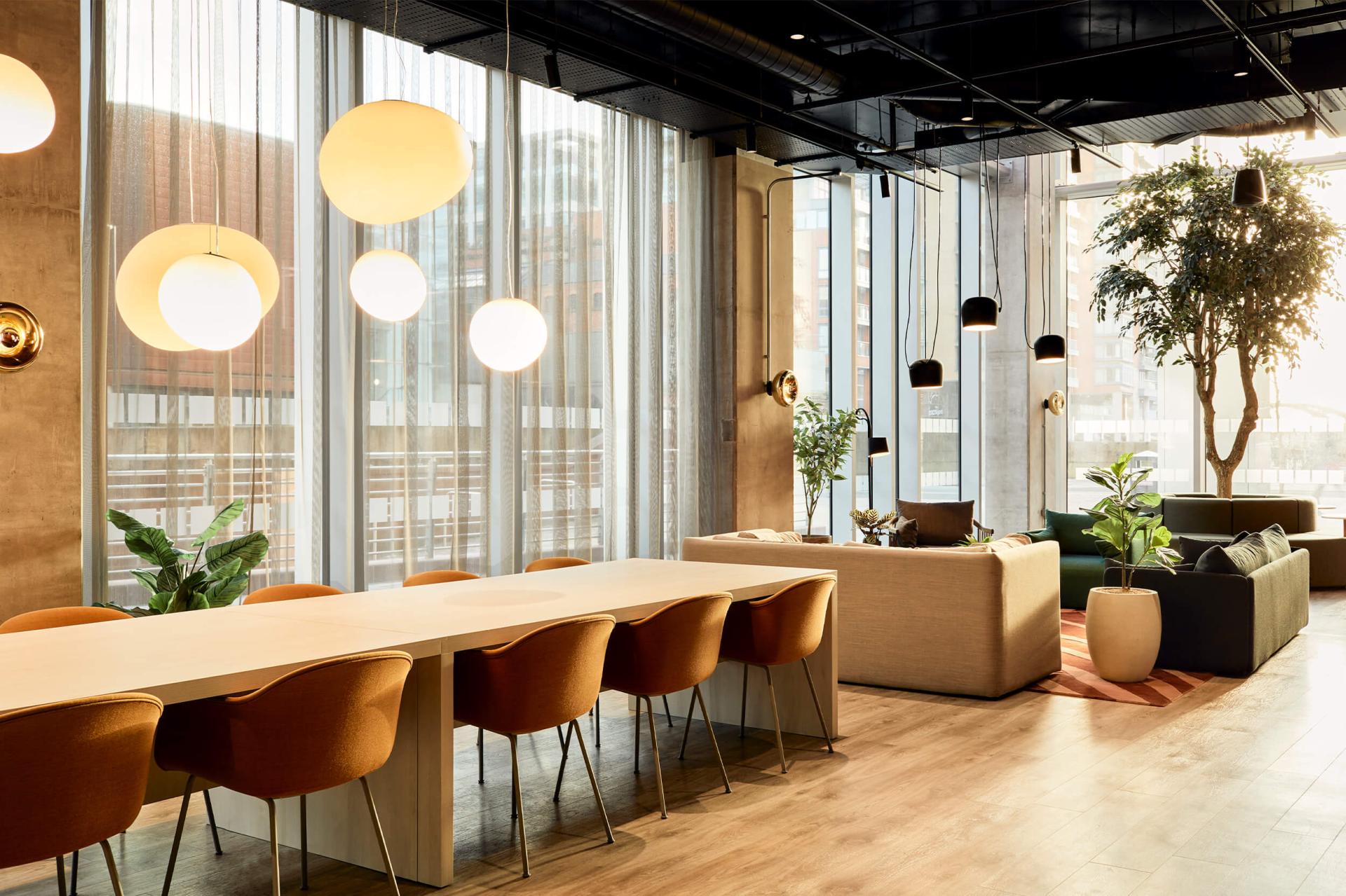 Brightly lit interior showcasing a modern design space with plants, a long dining table, and stylish seating arrangements.