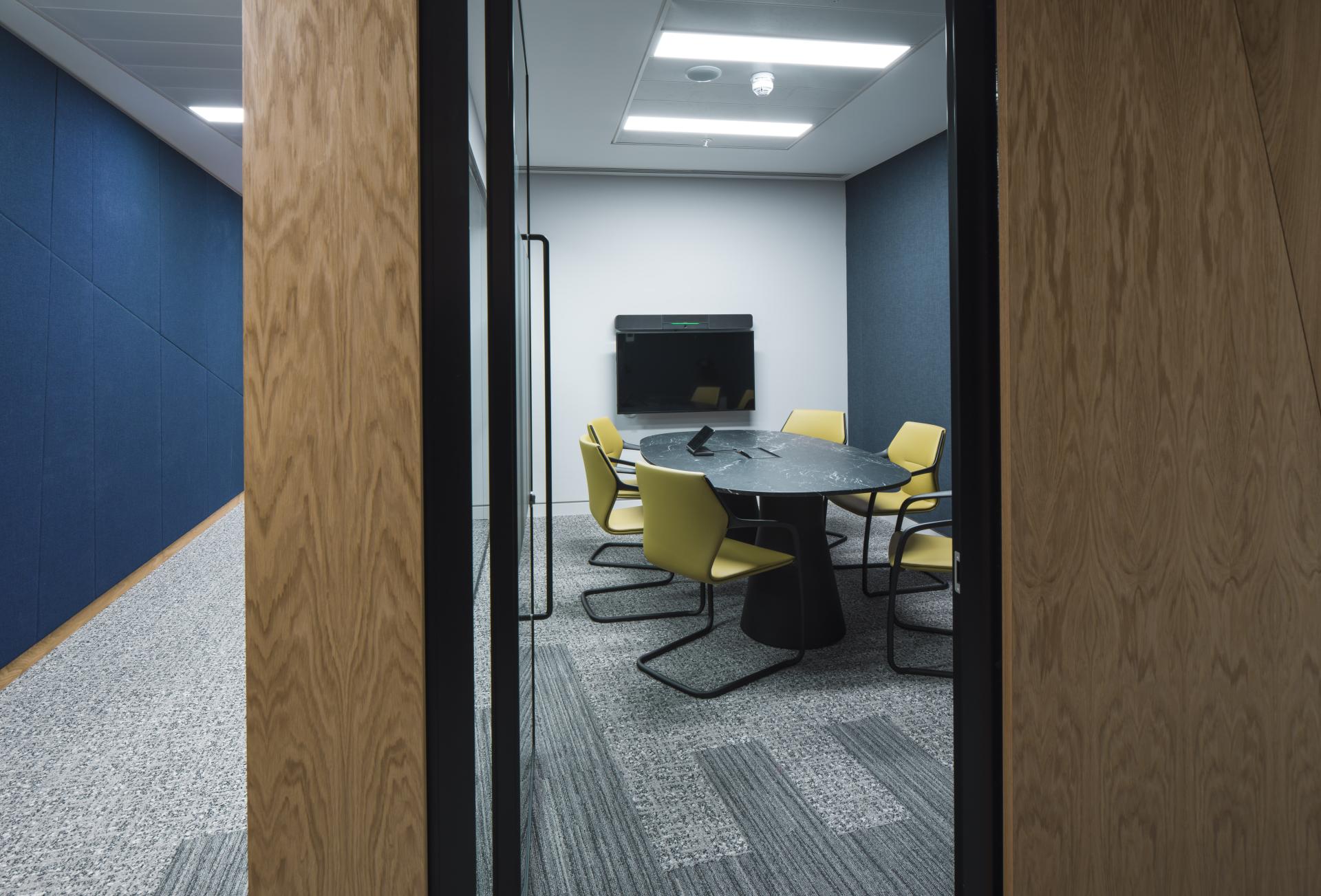 Modern conference room featuring a round table, yellow chairs, and a wall-mounted screen, highlighting sustainable office design.