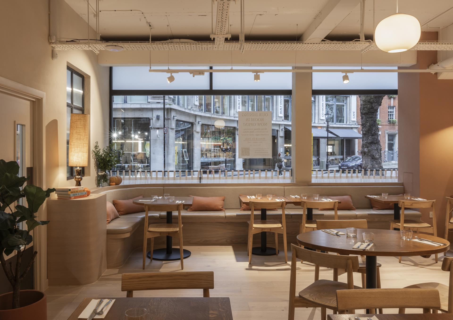 Modern deli interior featuring wooden tables, cozy seating, and large windows capturing an inviting atmosphere.
