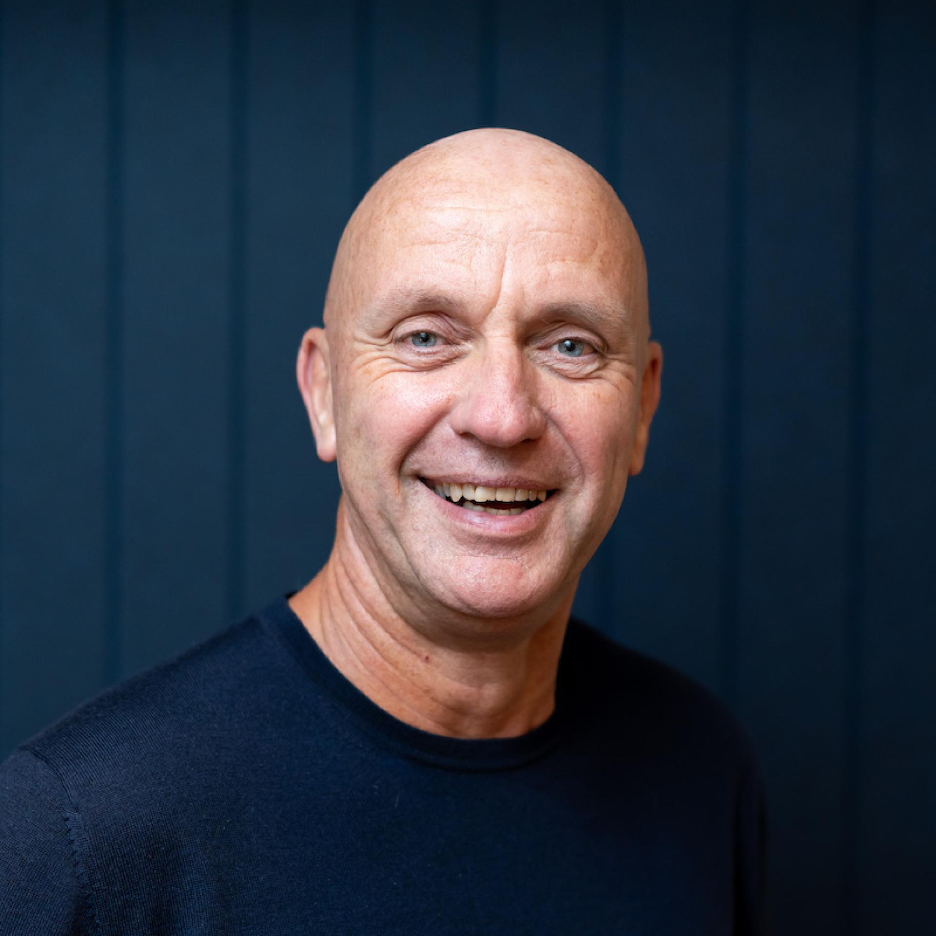 Smiling middle-aged man in a casual black shirt, representing modern workplace culture and diverse working environments.