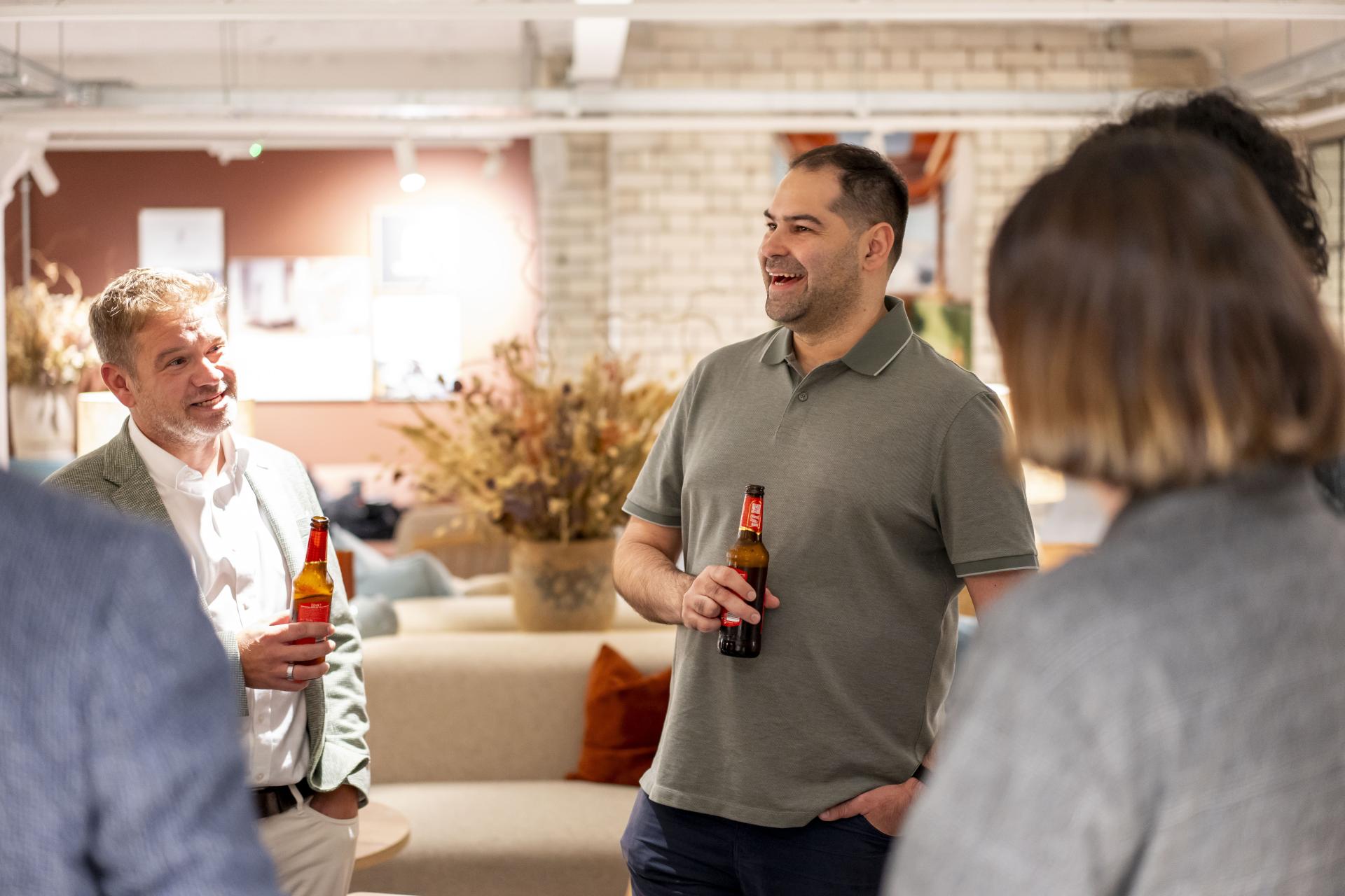 Group of colleagues engaging in conversation with drinks in a casual workspace, discussing technology's impact on the workplace.