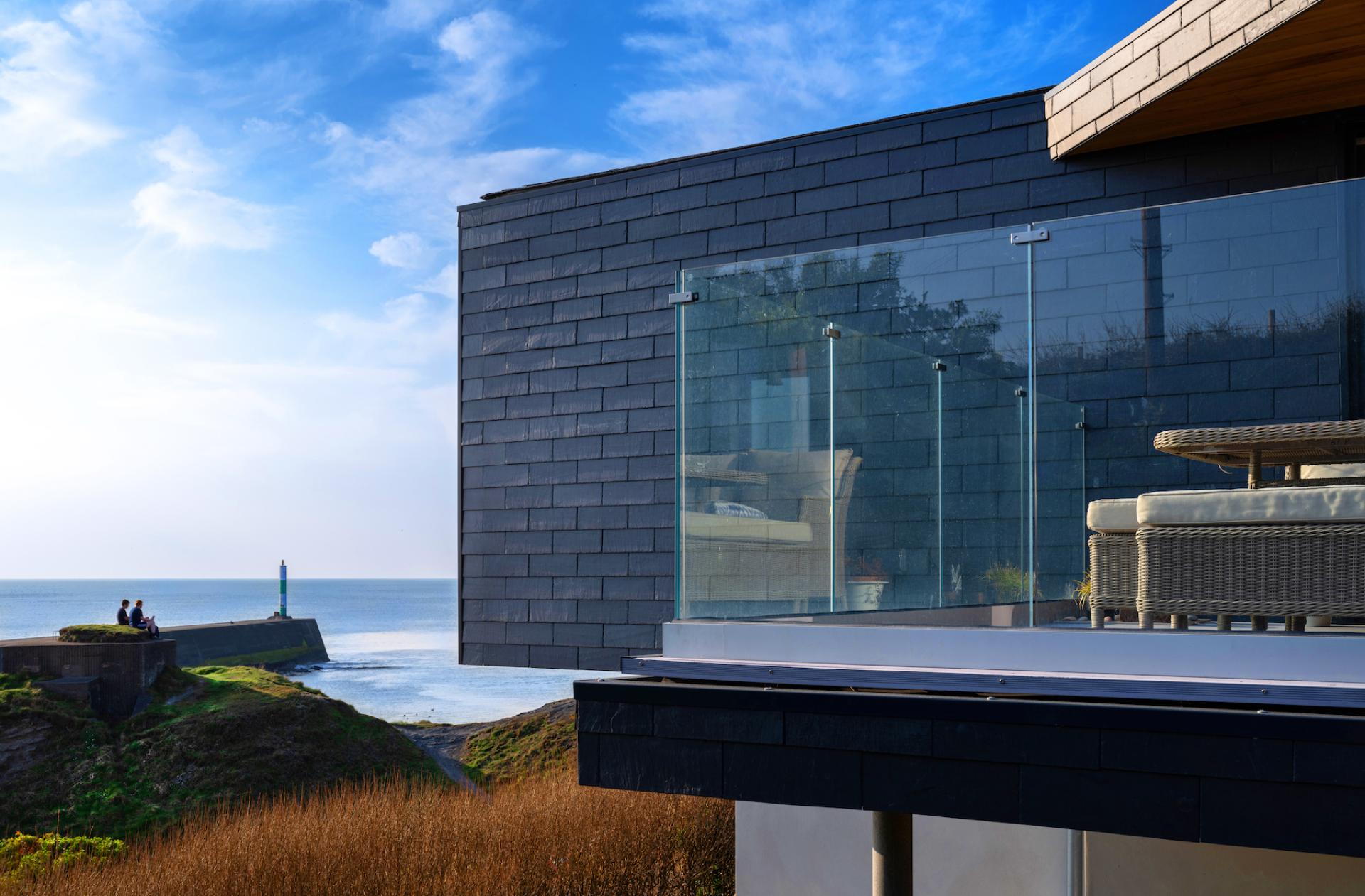 Modern coastal home featuring CUPACLAD 101 Logic slate cladding, glass balcony, and ocean view in the background.