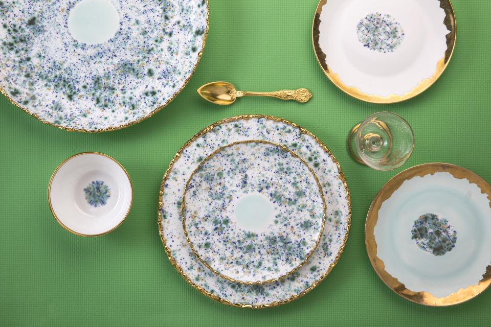 Hand-decorated ceramic and porcelain tableware by Coralla Maiuri, featuring vibrant colors and gold accents on a green background.