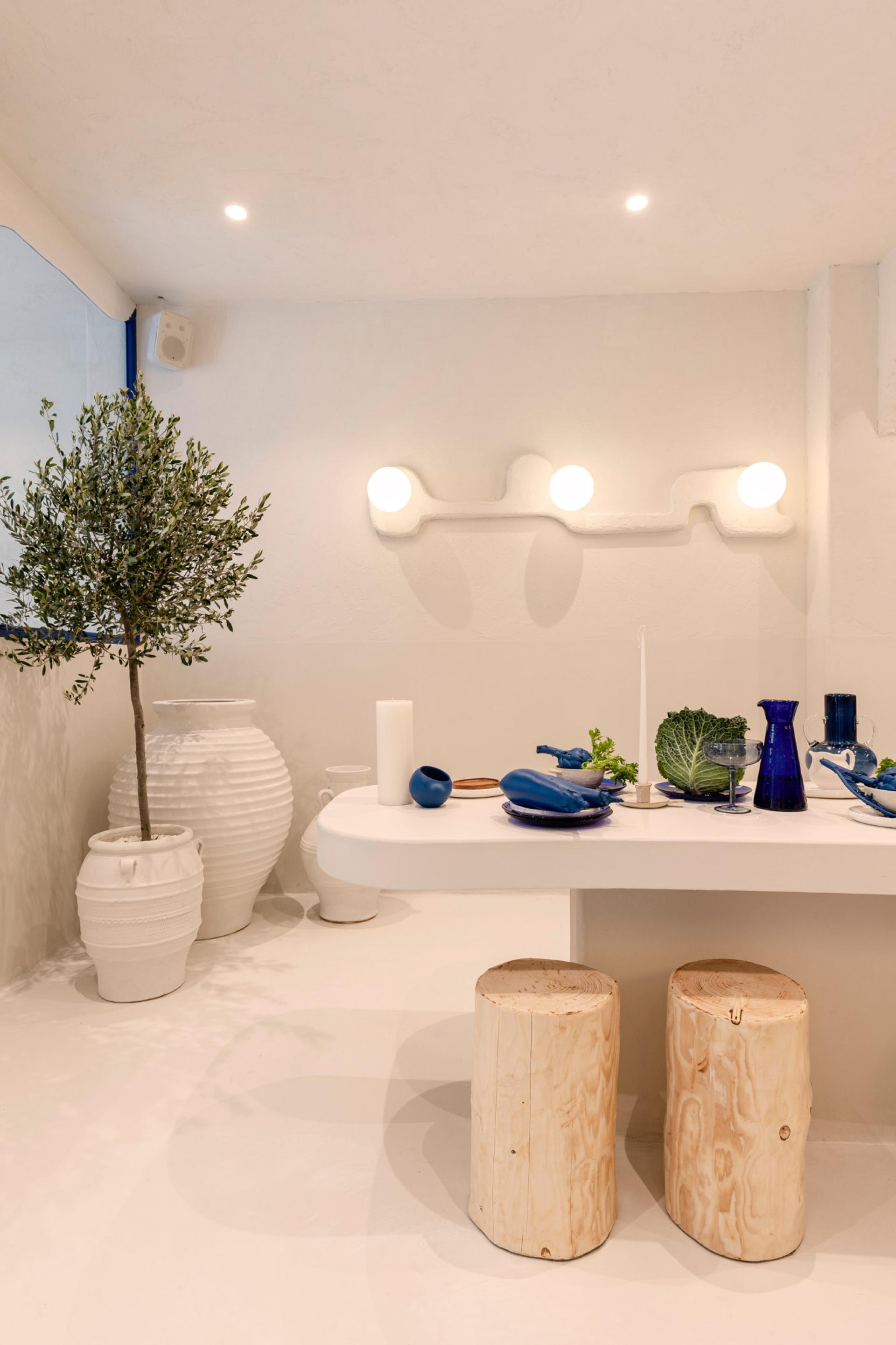 Modern Greek restaurant interior showcasing minimalist decor, olive tree, and traditional tableware designed by Masquespacio.