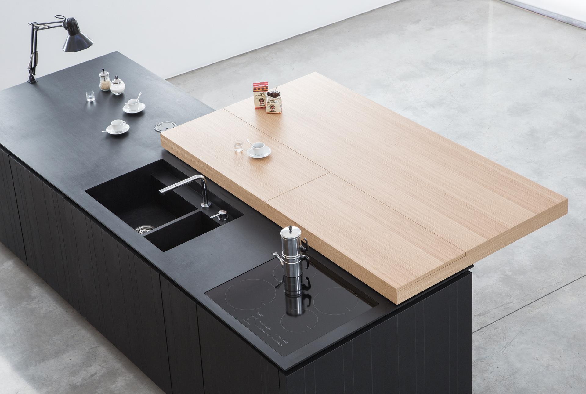 Modern kitchen island featuring black surface materials, wooden countertop, sink, and coffee setup, reflecting current design trends.