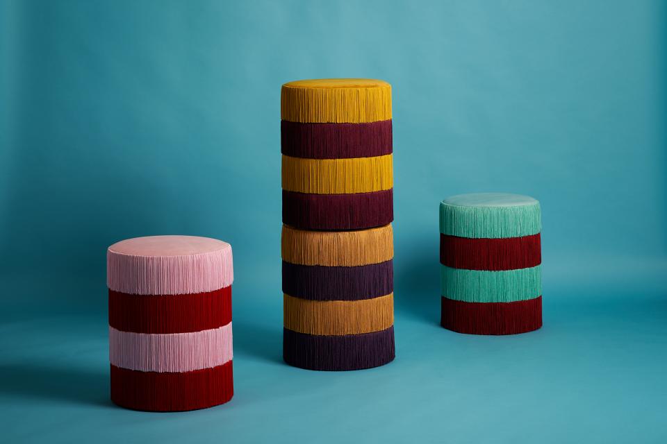 Vibrant, vintage-inspired stools in pink, red, yellow, green, and purple, showcasing unique fringe detailing against a blue backdrop.