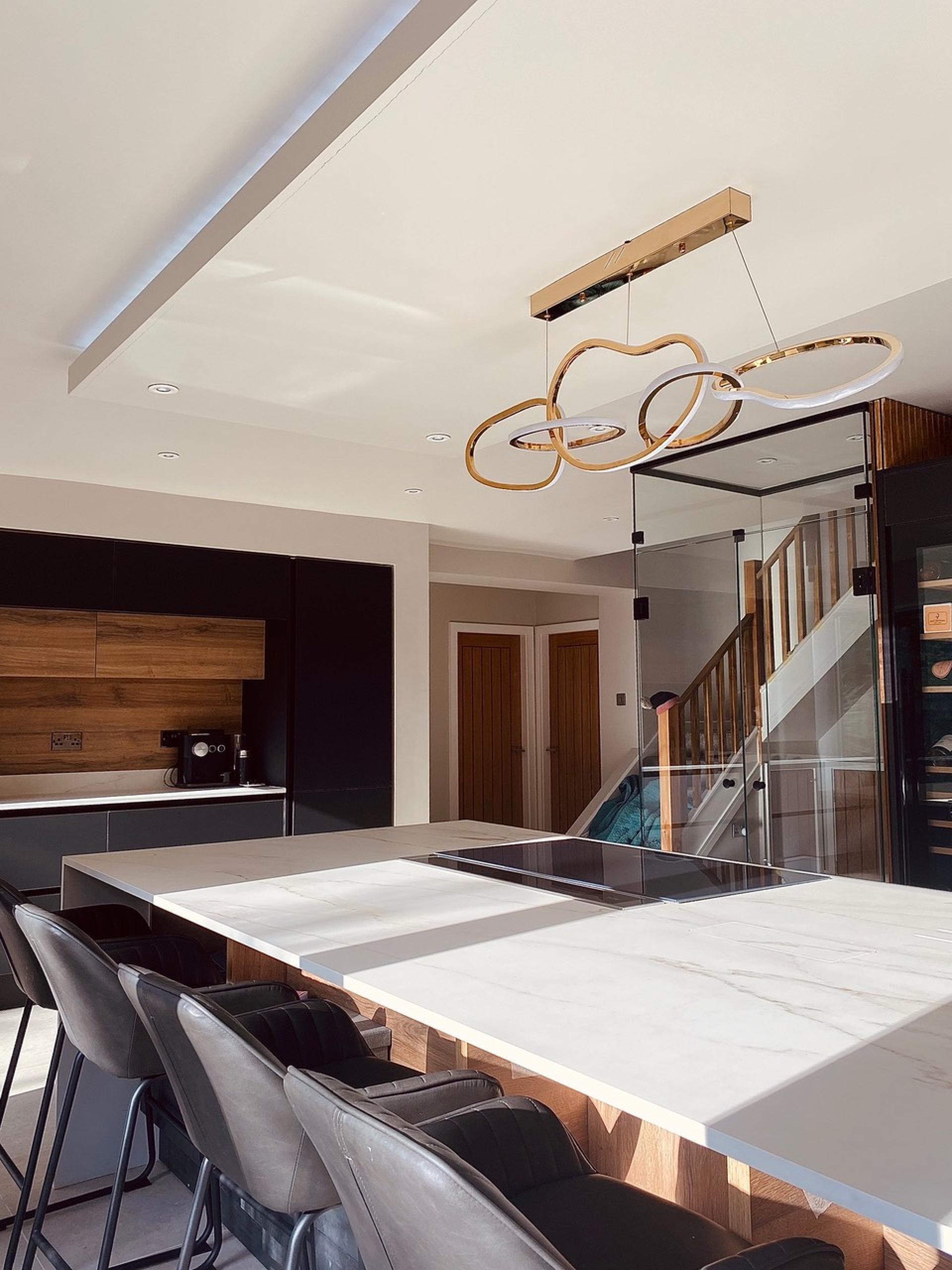 Elegant modern kitchen showcasing a large marble island, sleek black cabinetry, and stylish pendant lighting by Auric Design.