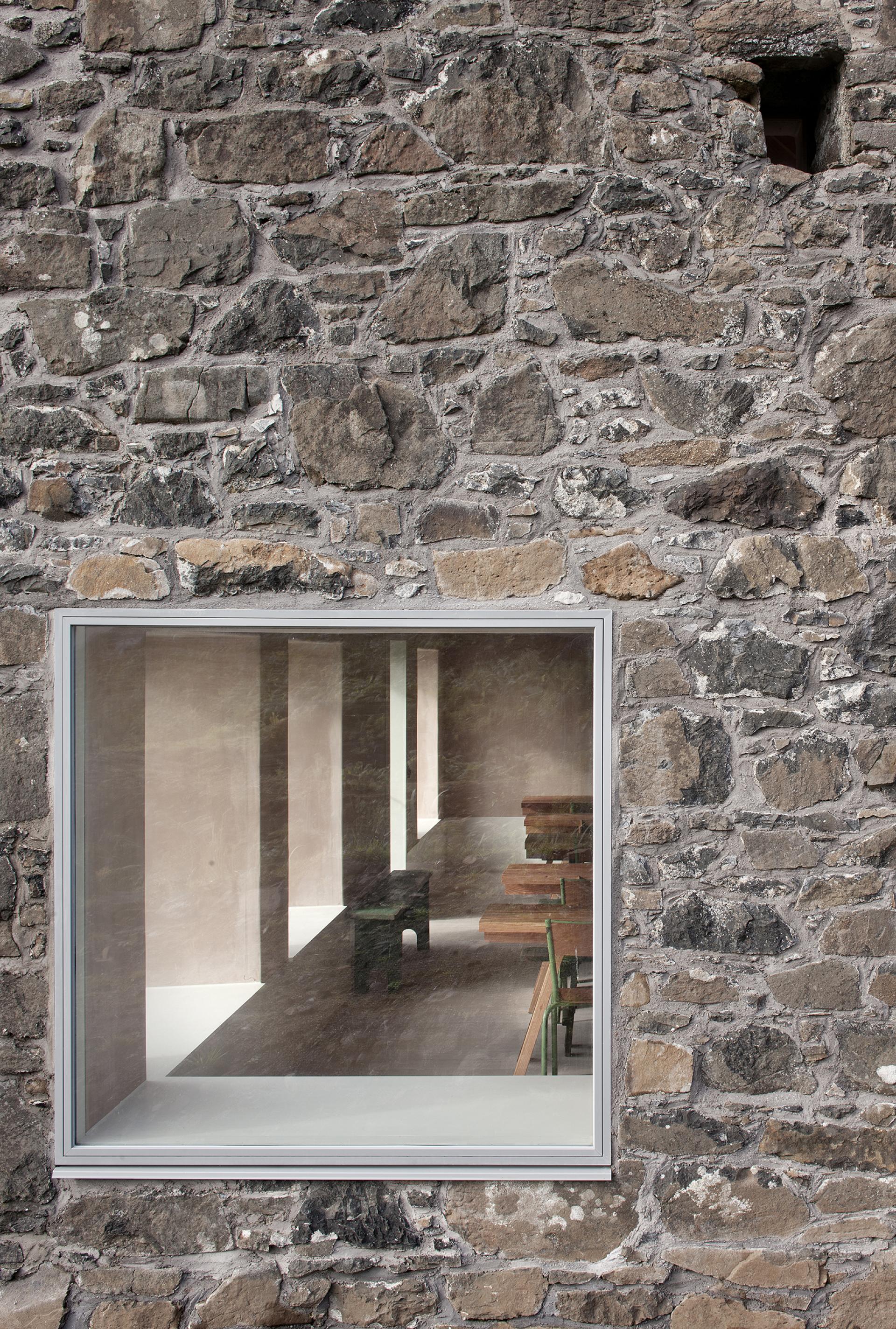 Restored stone wall of a croft with a modern window showcasing a minimalist interior and natural light.