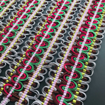 Vibrant hand-woven passementerie featuring intricate loops of colored threads in red, green, and silver.