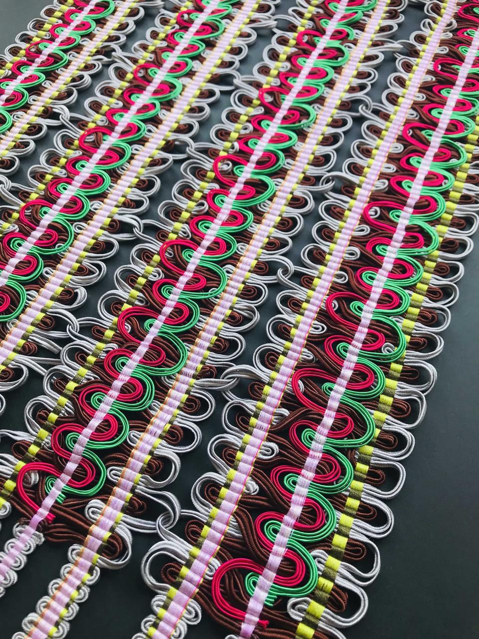 Vibrant hand-woven passementerie featuring intricate loops of colored threads in red, green, and silver.