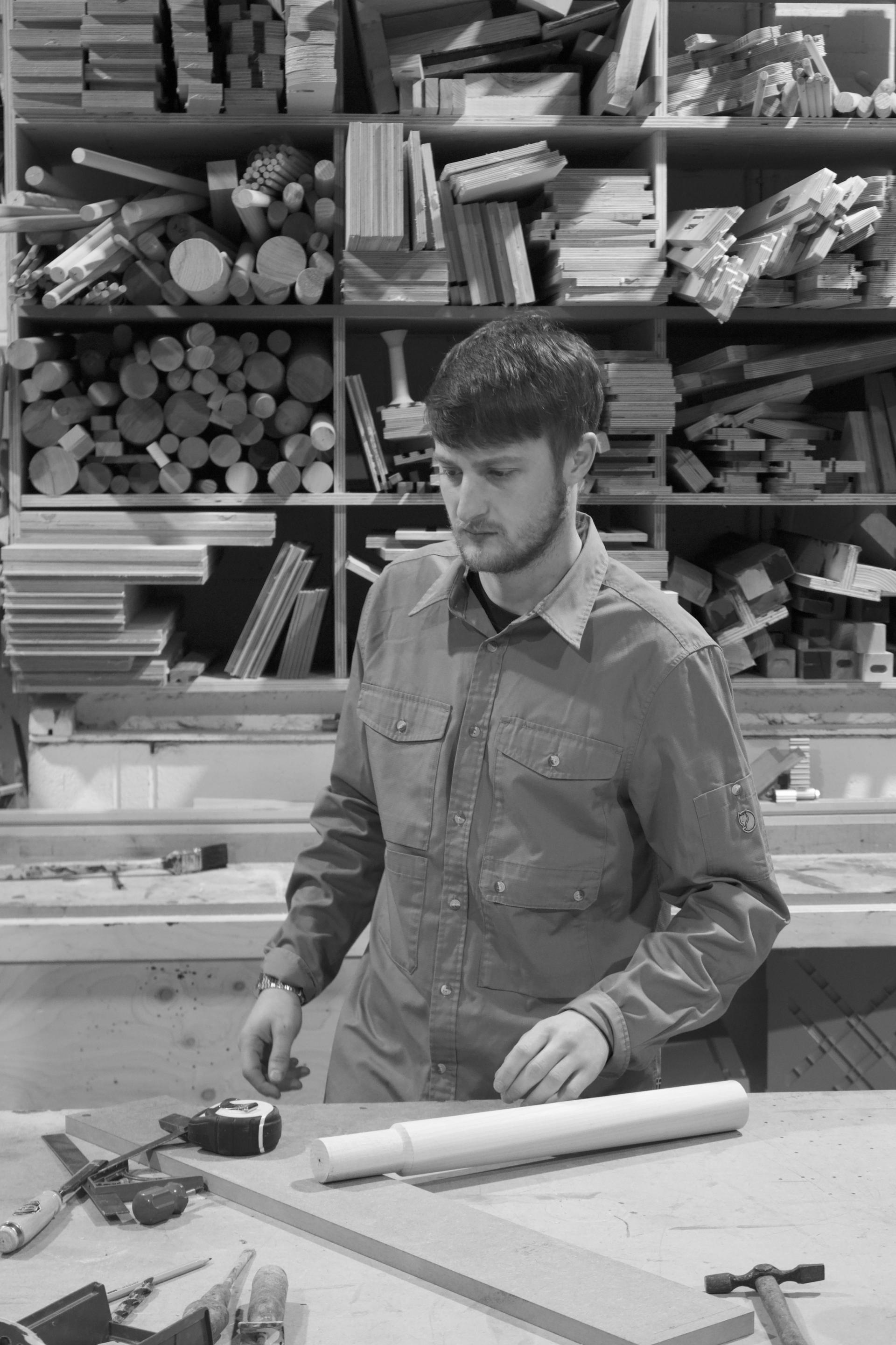 Jesse Cracknell working in a woodworking studio surrounded by various wood materials and tools, showcasing craftsmanship and creativity.