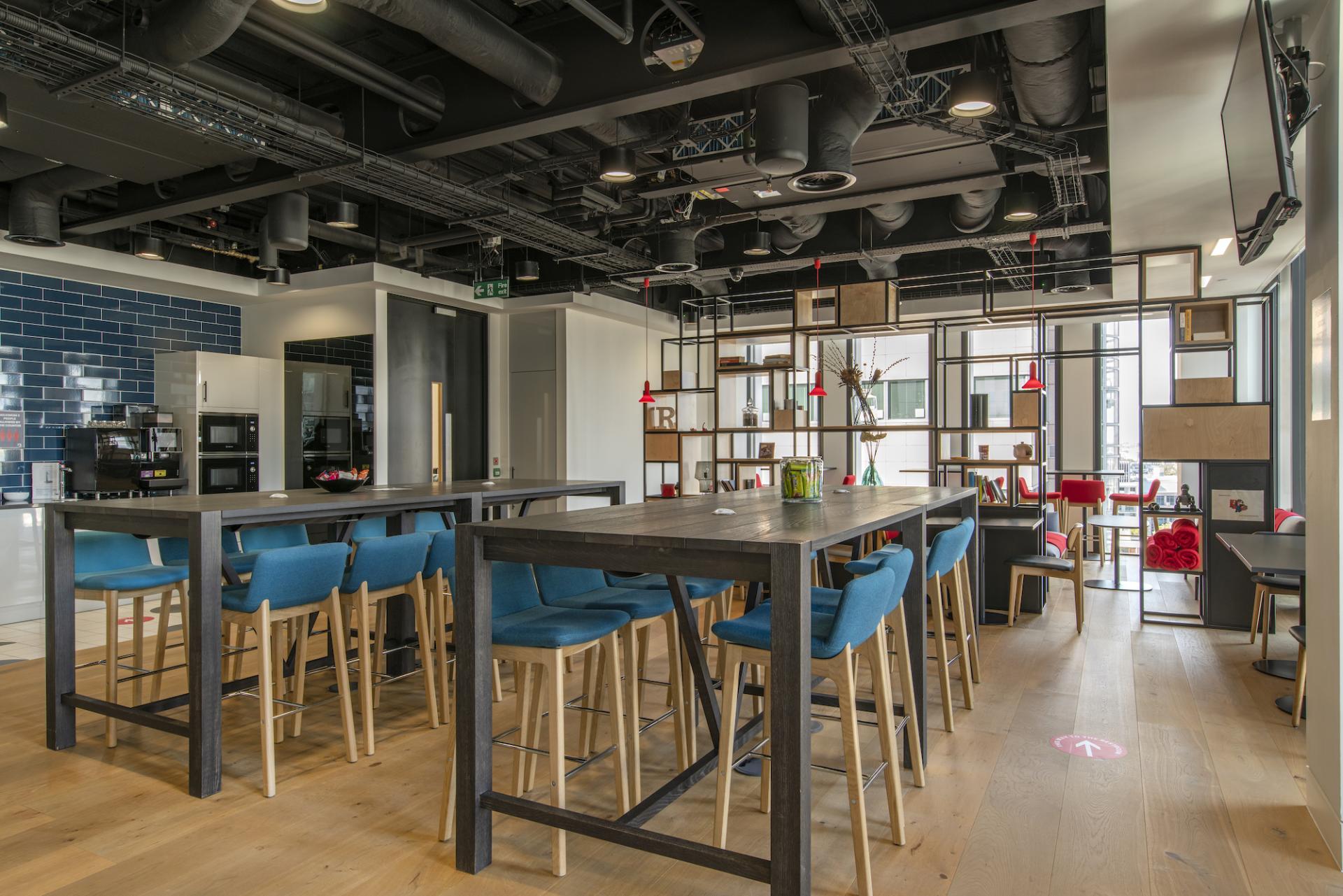 Modern office kitchen and lounge area featuring stylish furniture, vibrant blue seating, and a contemporary design aesthetic.