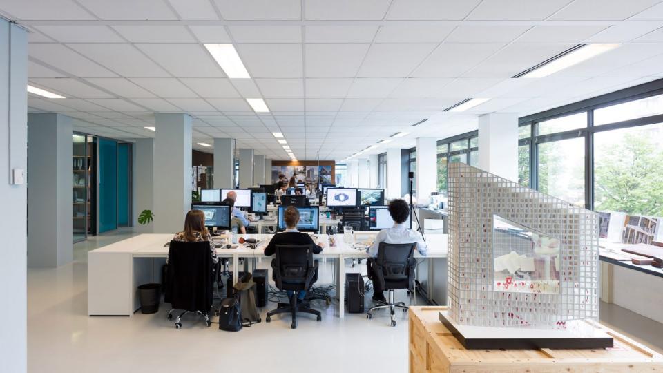 Modern architectural studio interior featuring designers at work and a prominent architectural model on display.