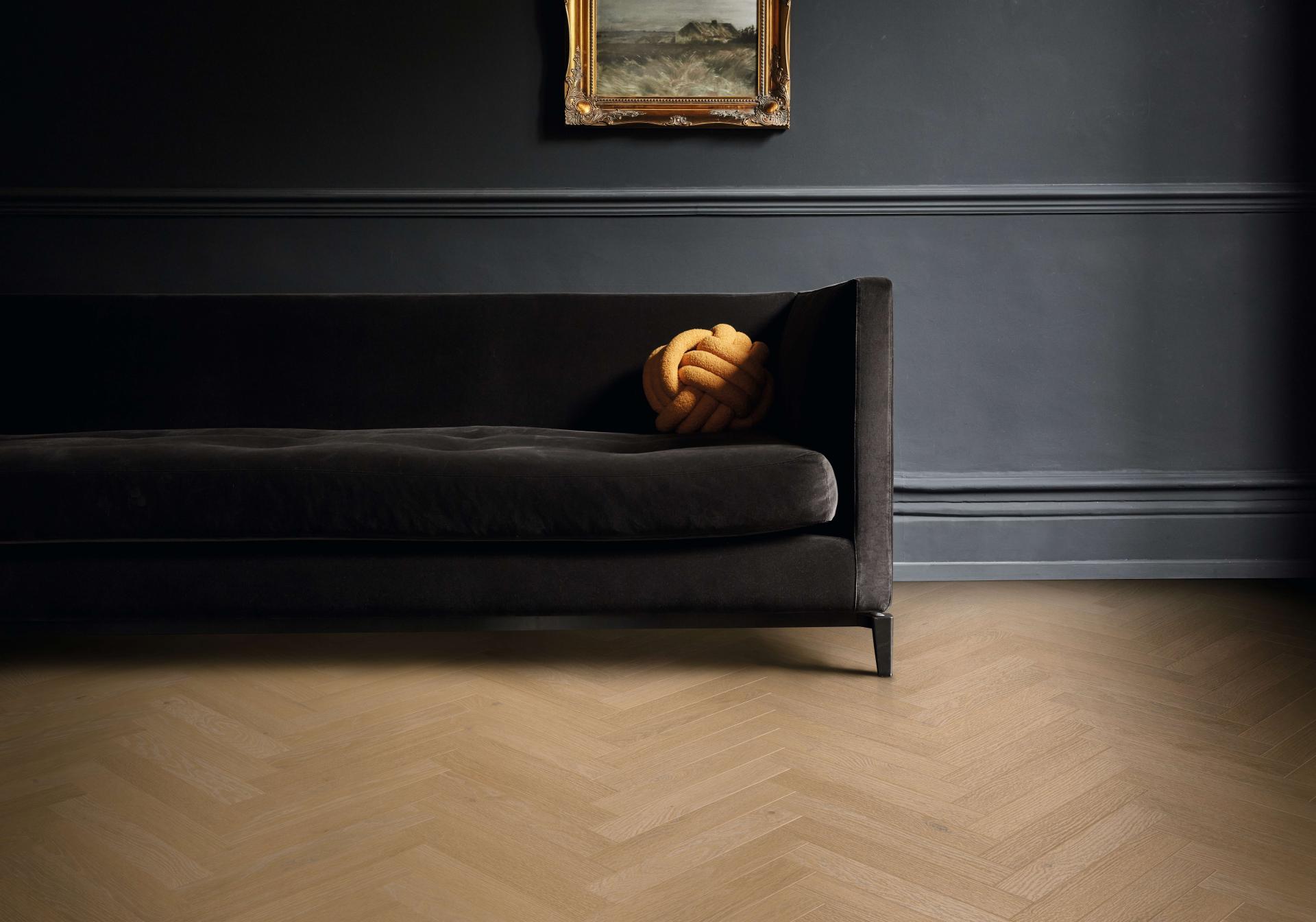 Elegant room showcasing Karndean's Art Select wood-inspired herringbone flooring, complemented by a dark velvet sofa and artistic decor.