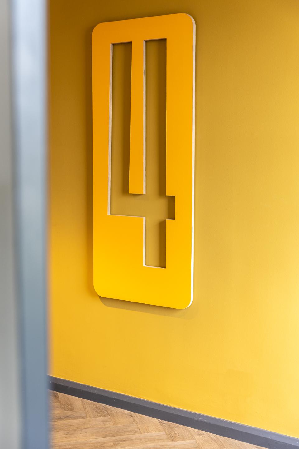 Bright yellow wall featuring a modern cutout sign displaying the number four in a stylish co-working space.