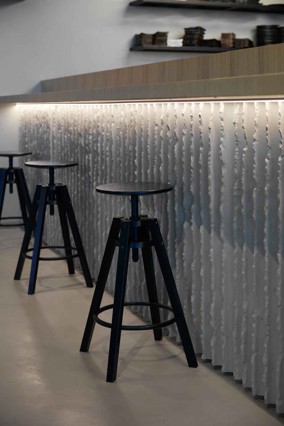 Stylish black stools lined against a textured wall, showcasing a chic interior design for Dubai's Origami restaurant.