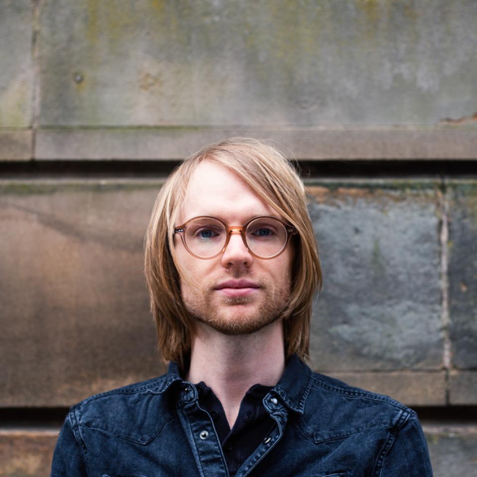 James Brimble, senior project architect at Page\Park, poses confidently against a stone wall in Glasgow.