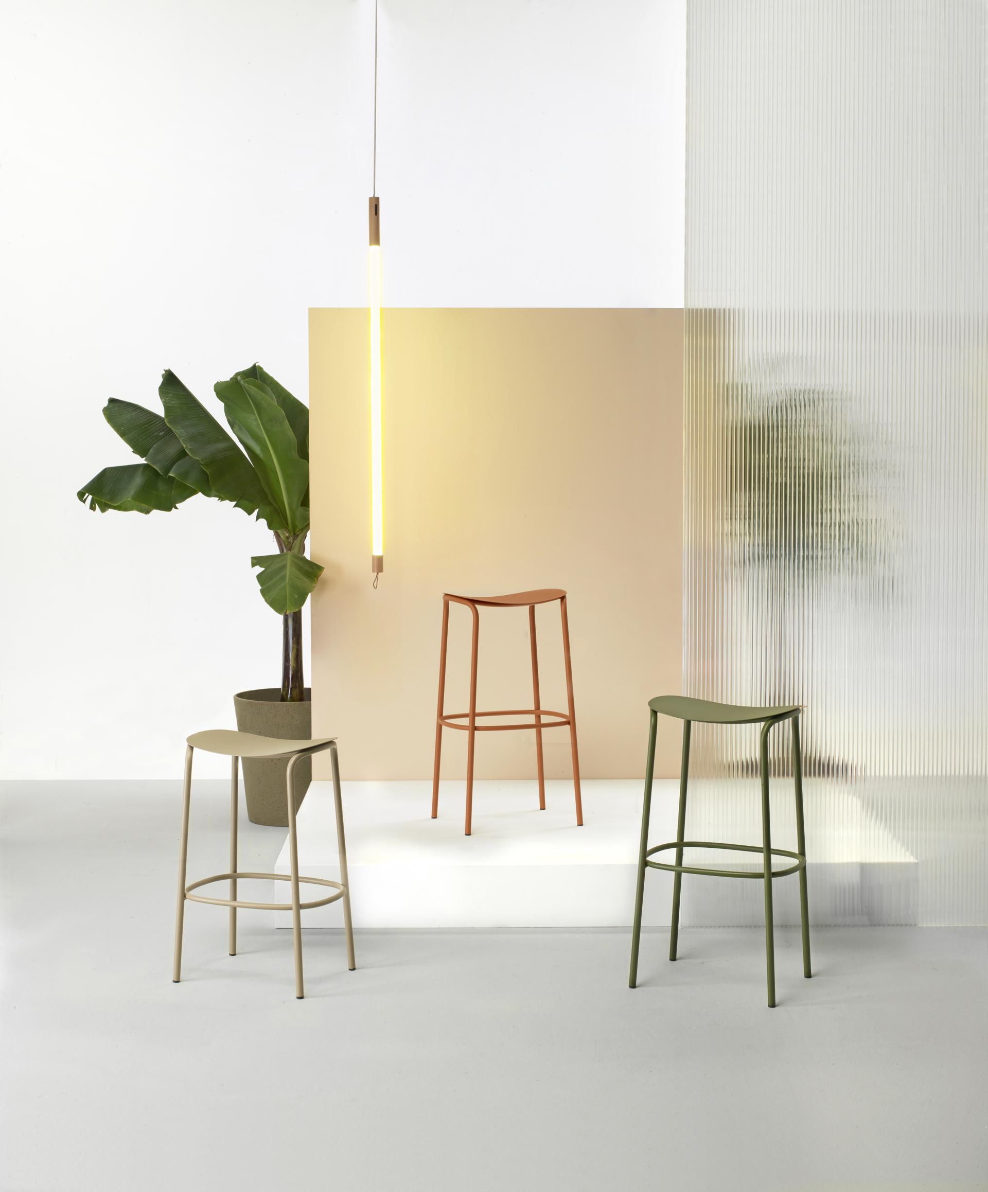 Modern indoor space featuring three minimalist bar stools in soft colors, complemented by stylish lighting and lush greenery.