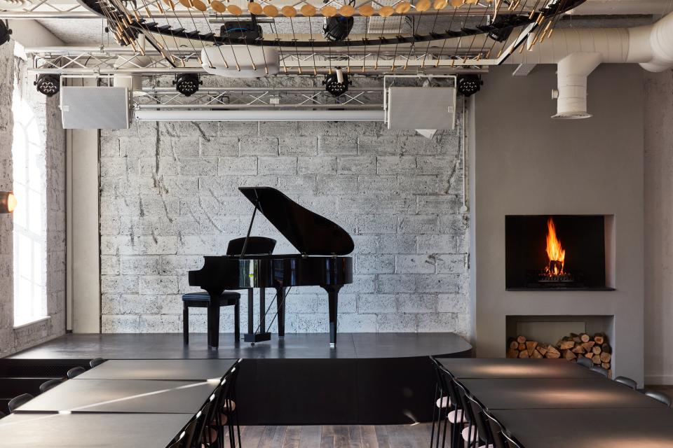 Elegant co-working space featuring a grand piano, stage, and modern decor inspired by cocktail bar aesthetics in London.