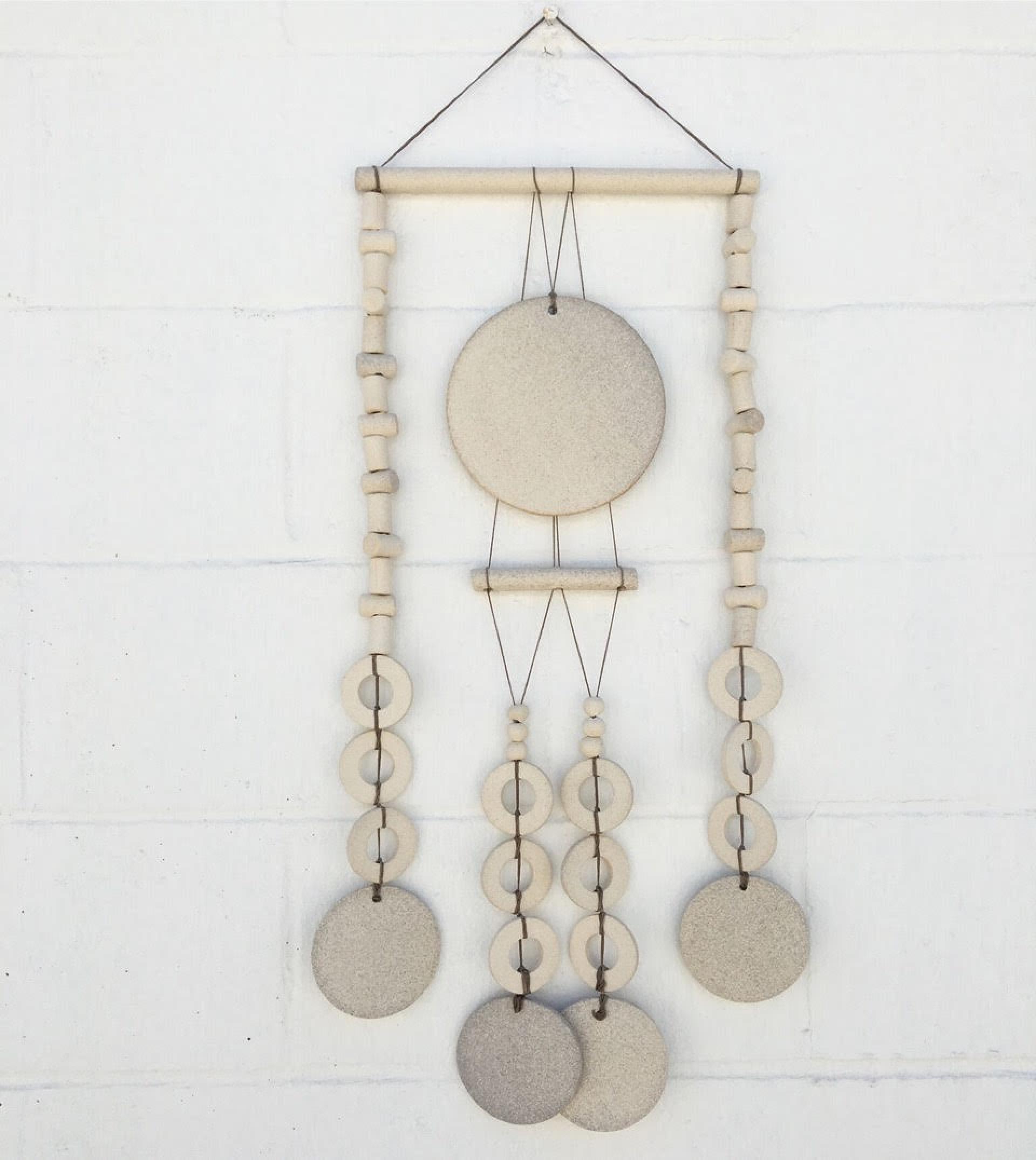 Wall hanging made of beige stoneware featuring circular elements, showcasing Heather Levine's unique ceramic art style.