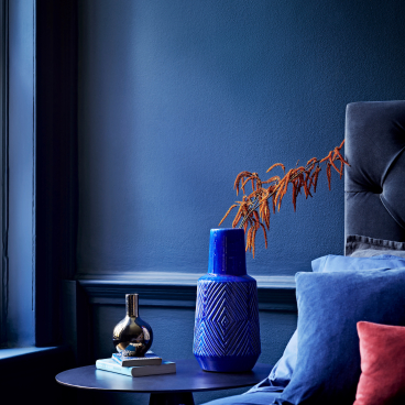 Stylish bedroom corner featuring blue walls, decorative vases, and vibrant cushions, showcasing Crown Paints' color impact.