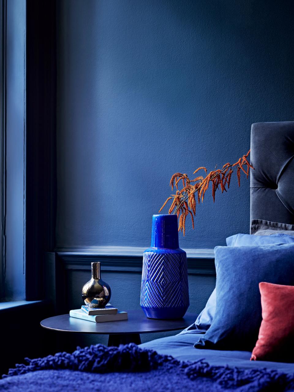 Stylish bedroom corner featuring blue walls, decorative vases, and vibrant cushions, showcasing Crown Paints' color impact.