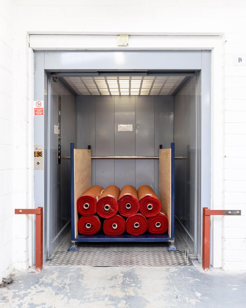 Elevator interior showcasing neatly stacked rolls of vibrant red upholstery fabric at Kvadrat's textile facility.