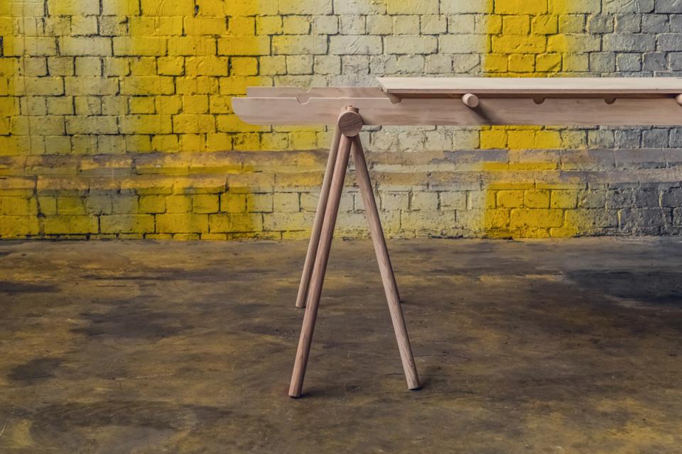 Flexible wooden table design by Tim Denton, set against a colorful brick wall, ideal for pop-up shops.