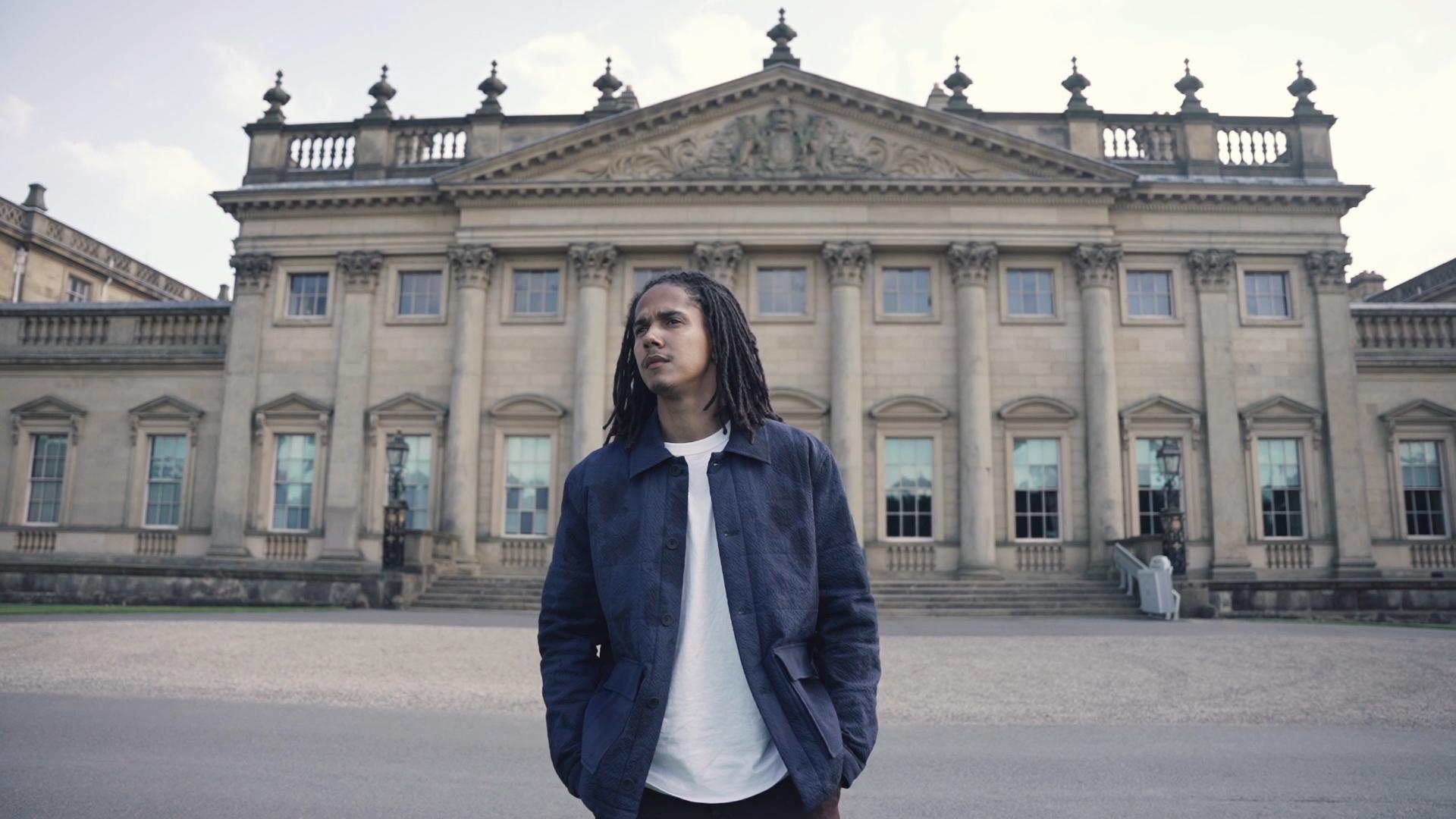 Young man standing in front of a historic mansion, representing themes of social and environmental purpose at Harewood Biennial 2022.