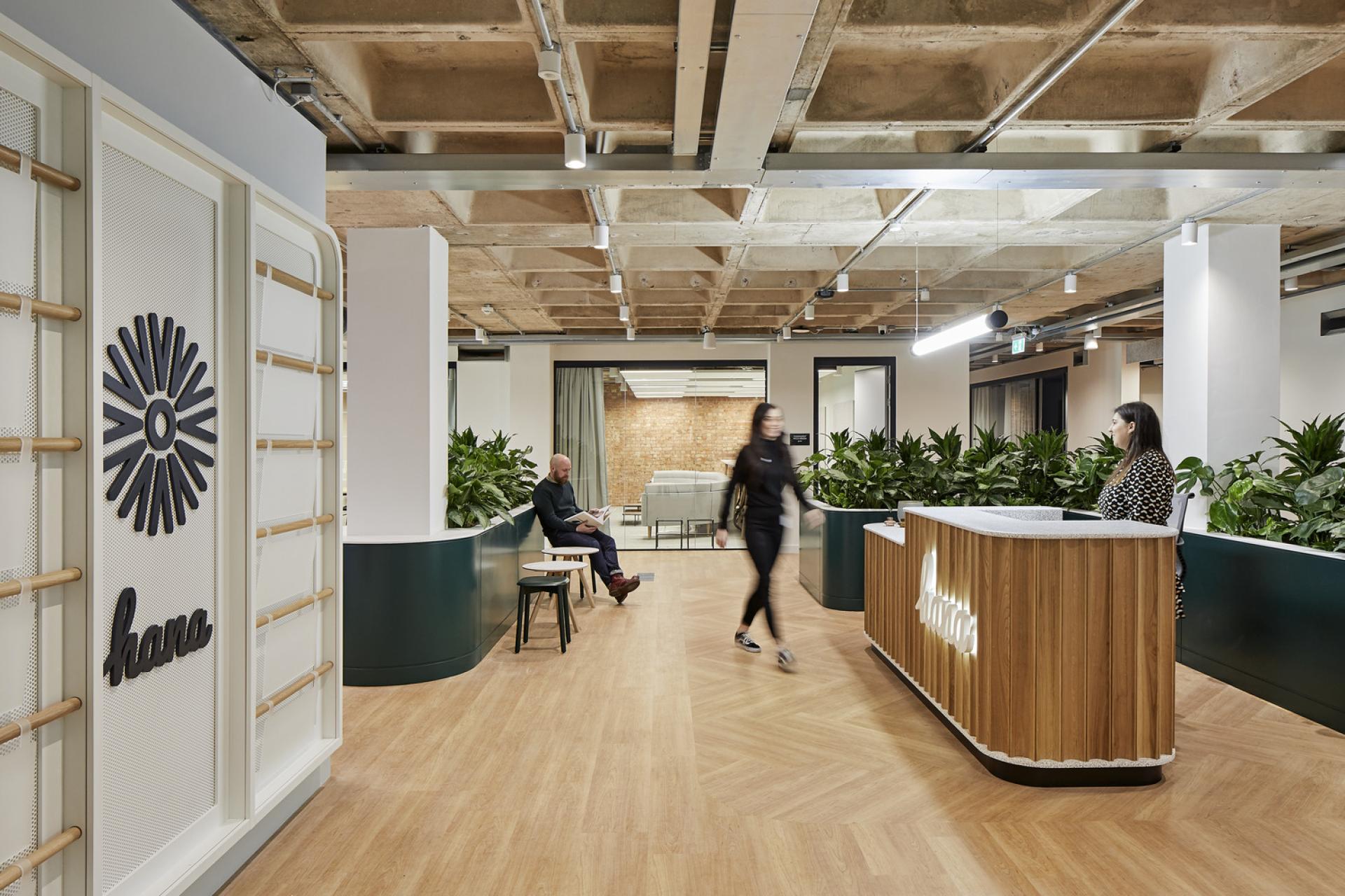 Modern office interior featuring a reception area, greenery, and people engaging in a creative workspace.