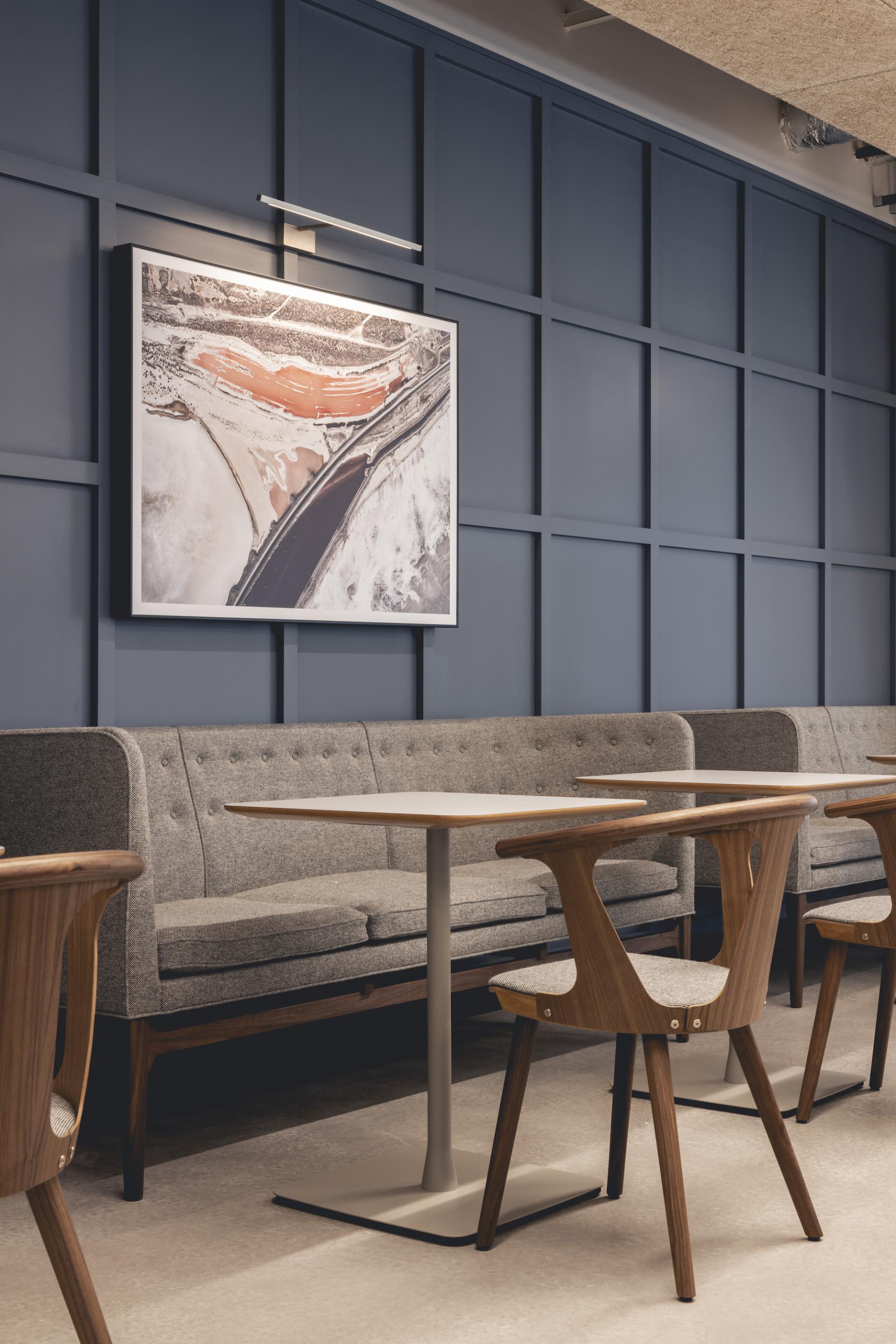Modern workplace design showcasing a cozy seating area with gray upholstery, wooden chairs, and an artistic wall display.