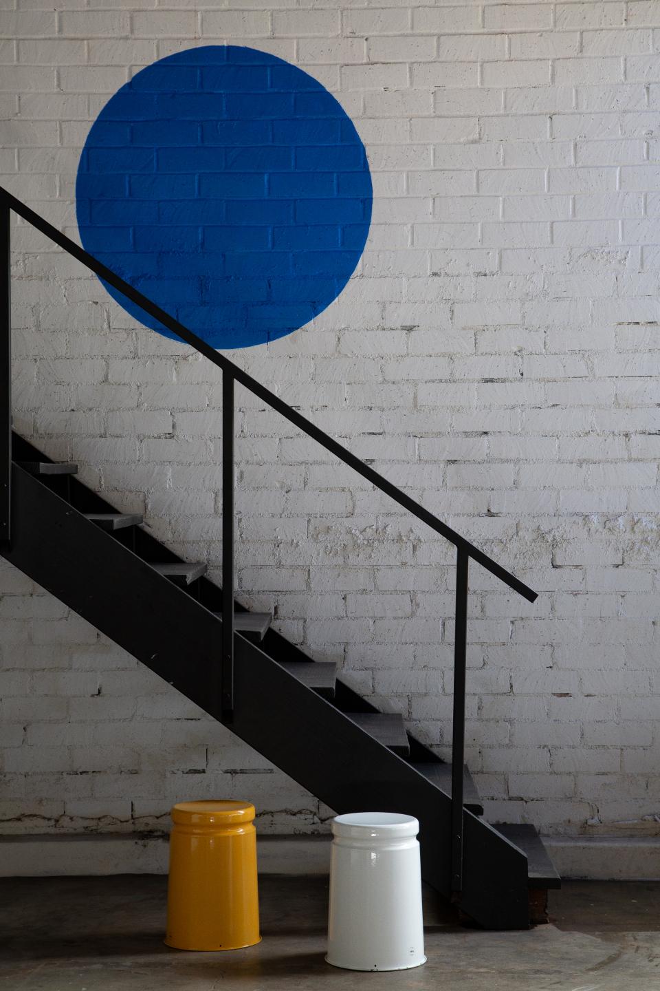 Colorful stools stand beneath a blue circle mural in Hem's new Los Angeles showroom, showcasing modern design elements.