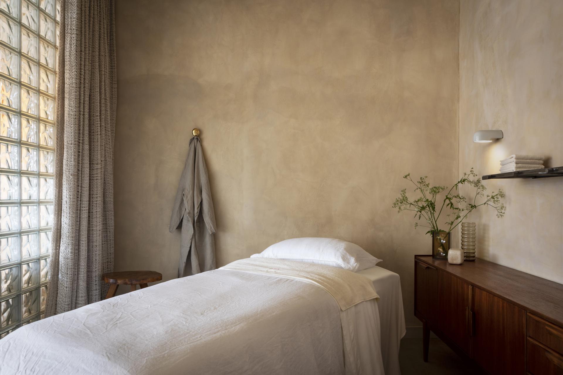 Serene interior of a minimalist spa room featuring natural materials, a bed, and elegant decor emphasizing sustainability.