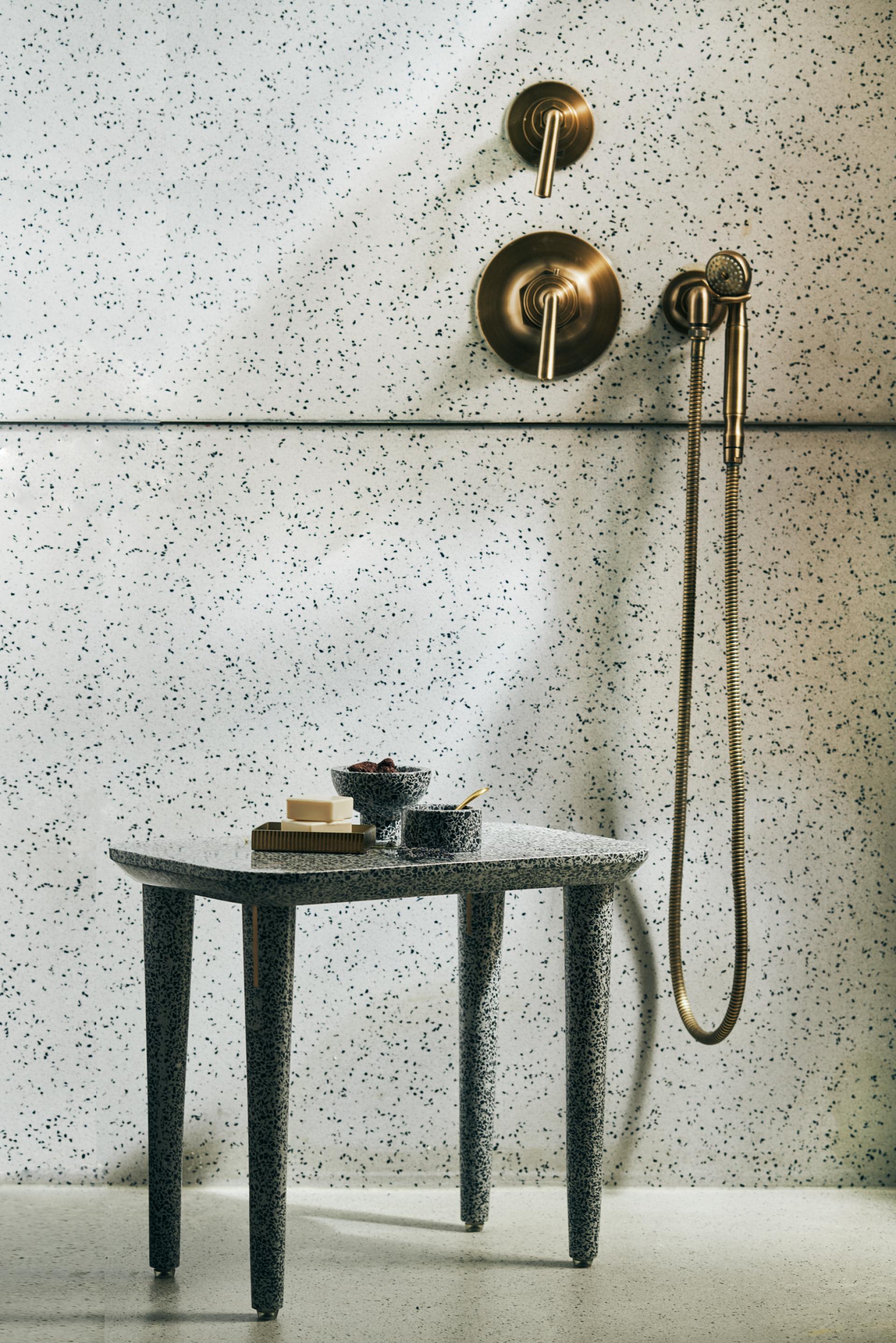 Terrazzo table with rounded edges, adorned with bowls and soaps, against a speckled wall featuring brass fixtures.