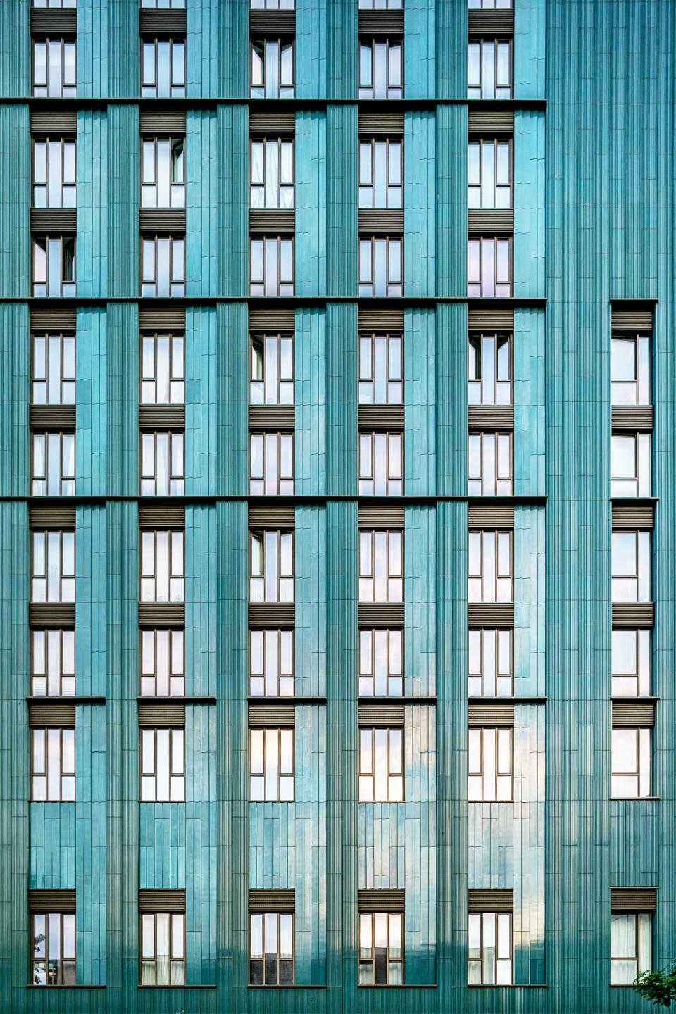 Modern architectural facade featuring turquoise ceramic tiles and a rhythmic pattern of windows, embodying the ceramic renaissance.