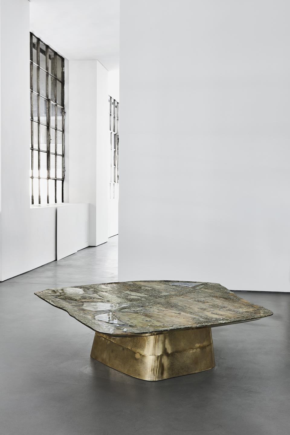 Sculptural coffee table with a textured stone top and a luxurious brass base, featured in Vincenzo de Cotiis' design exhibition.