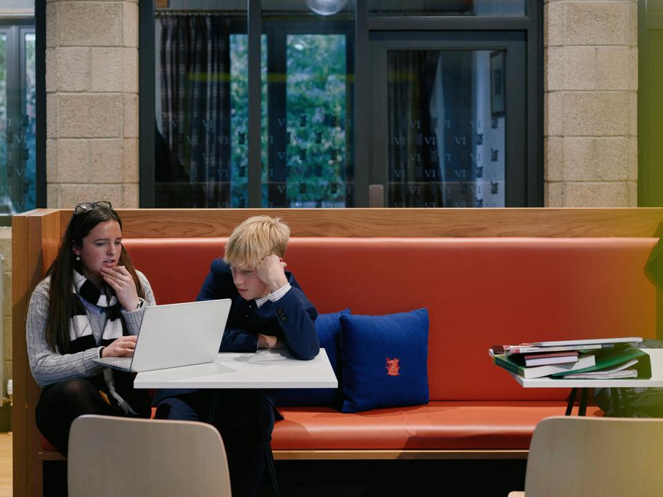 Students collaborate on a laptop in a modern seating area at Sedbergh School's Queens Hall, showcasing vibrant design and rich textures.