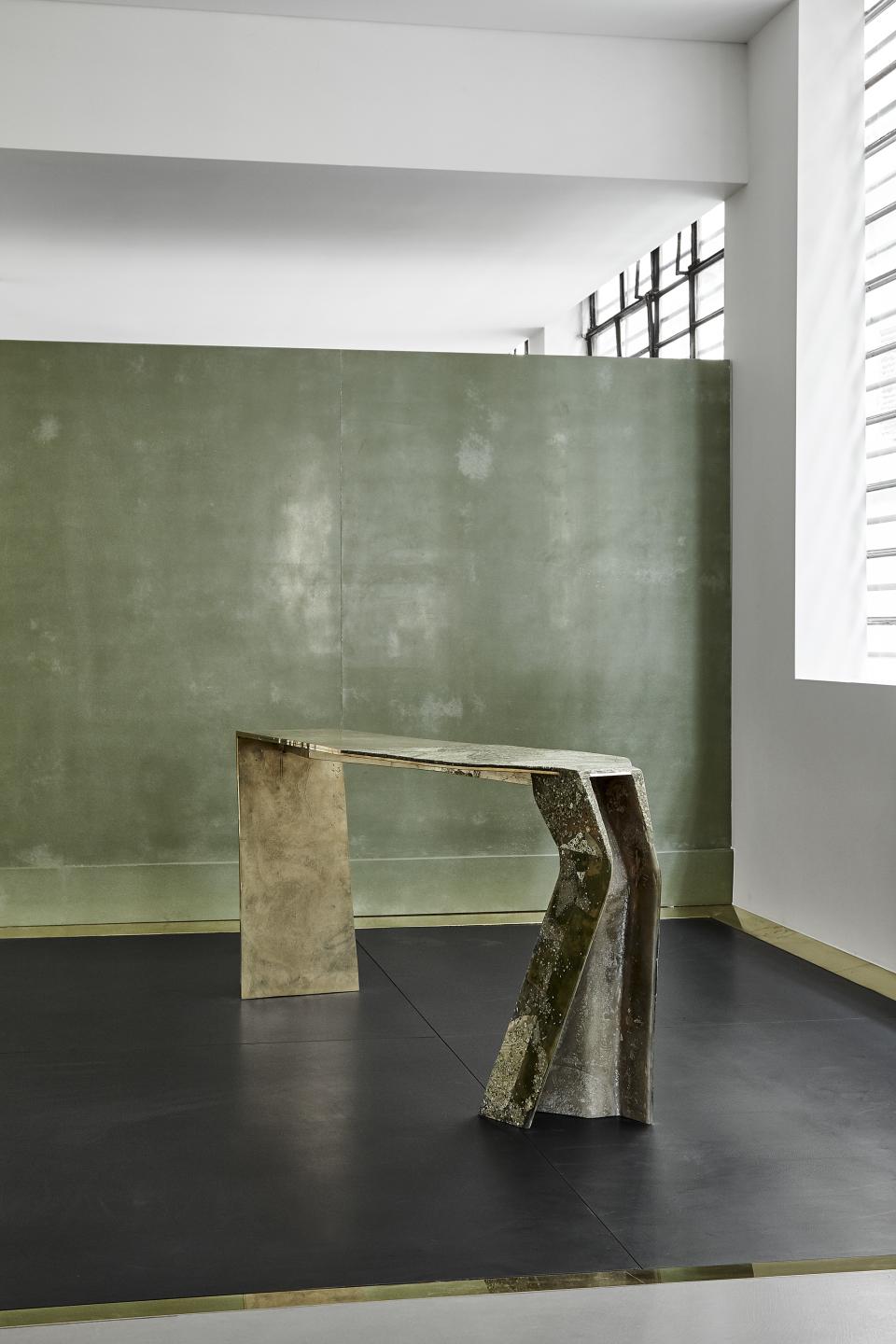 Sculptural table by Vincenzo de Cotiis featuring opulent materials, set against a minimalist green background in a gallery space.
